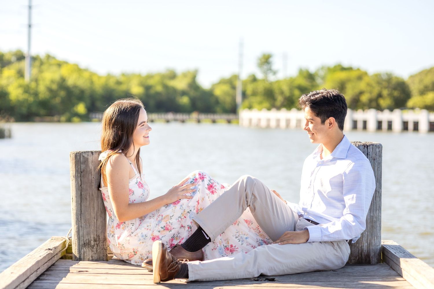 Golden hour engagement photo of a couple sitting on the dock at White Rock Lake in Dallas smiling at one another