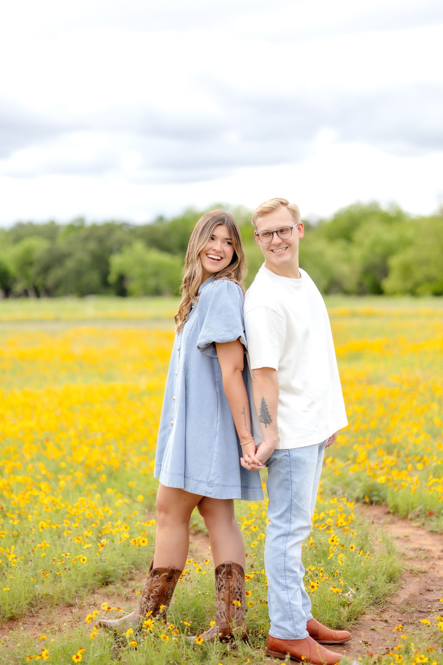married couple standing back to back in a wildflower field with yellow flowers and looking over their shoulders at each other