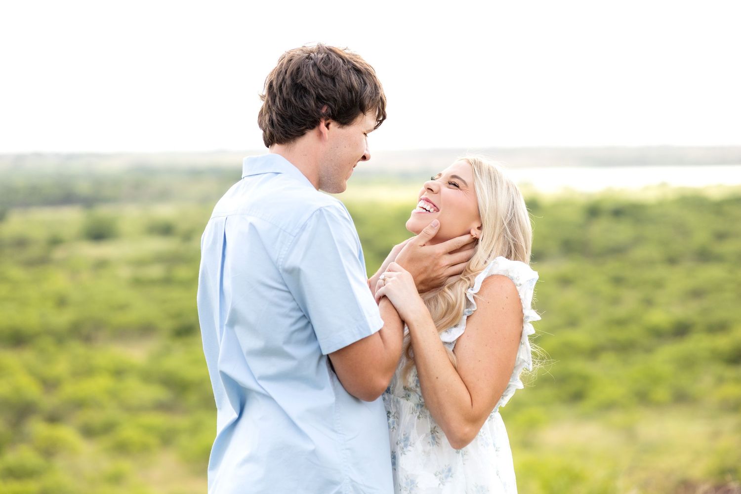 Engaged man holding his fiancé's face as she laughs during Texas engagement photo session on a ranch