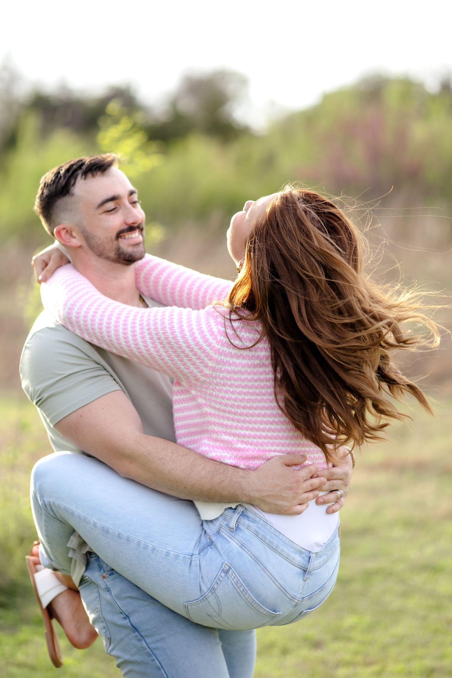 Man picking up his wife and spinning her around in a field at golden hour in Dallas, Texas