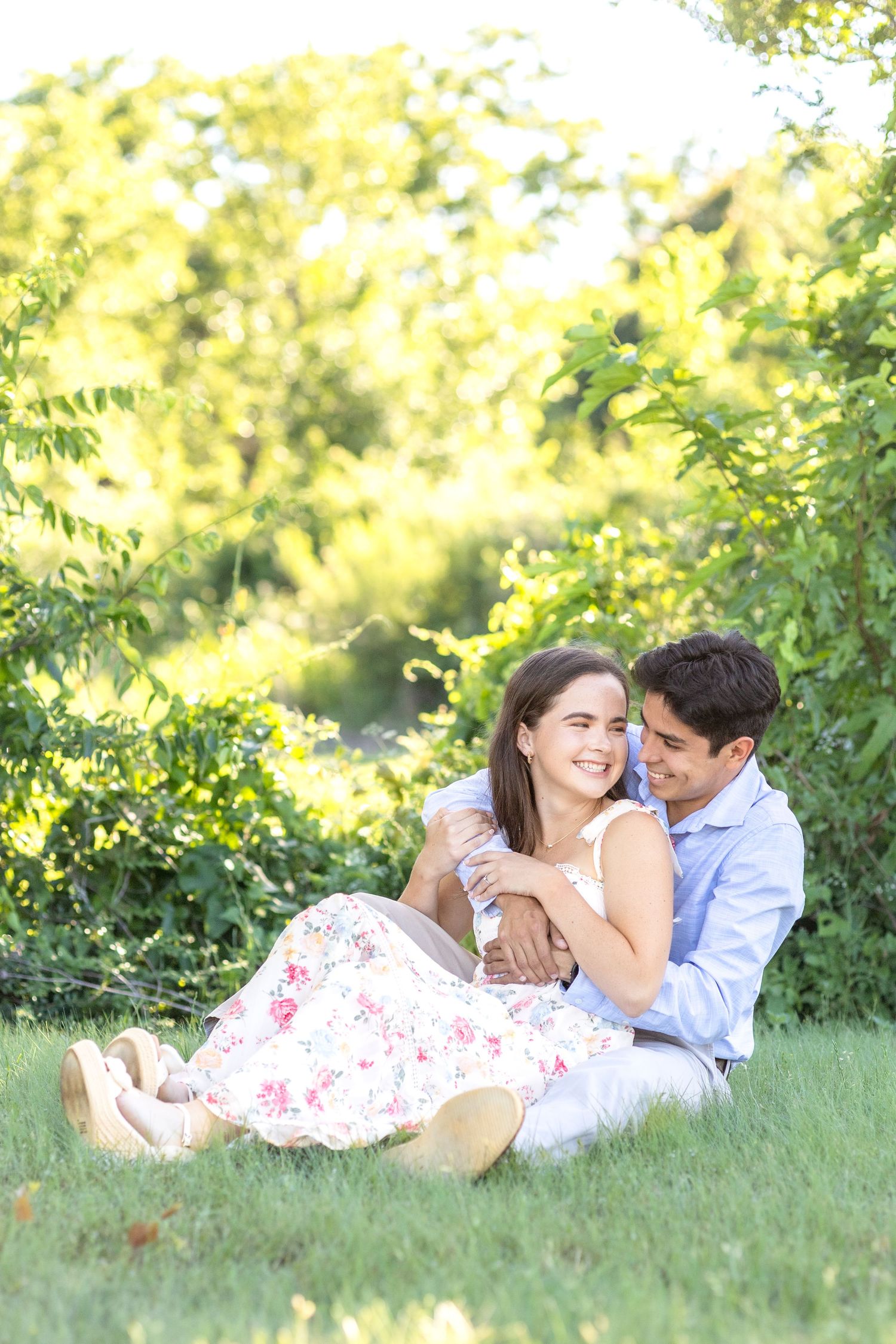 Engaged couple sitting together in the grass and wrapped up in a hug at White Rock Lake