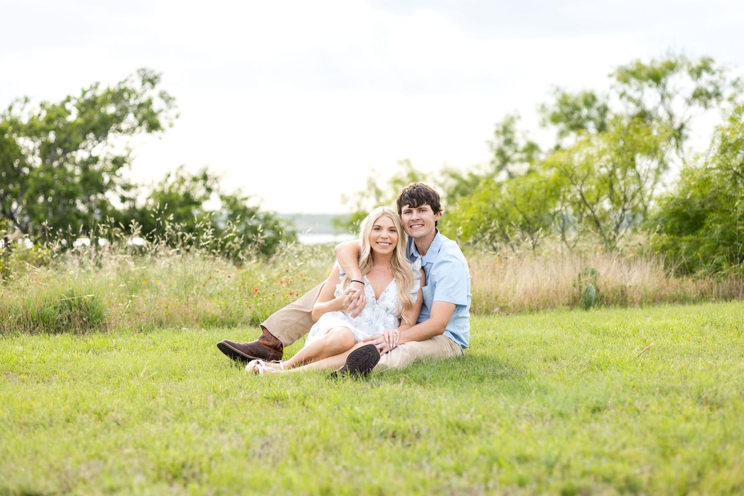 Engaged couple sitting in a field and smiling during sunset engagement photo session on a Texas ranch