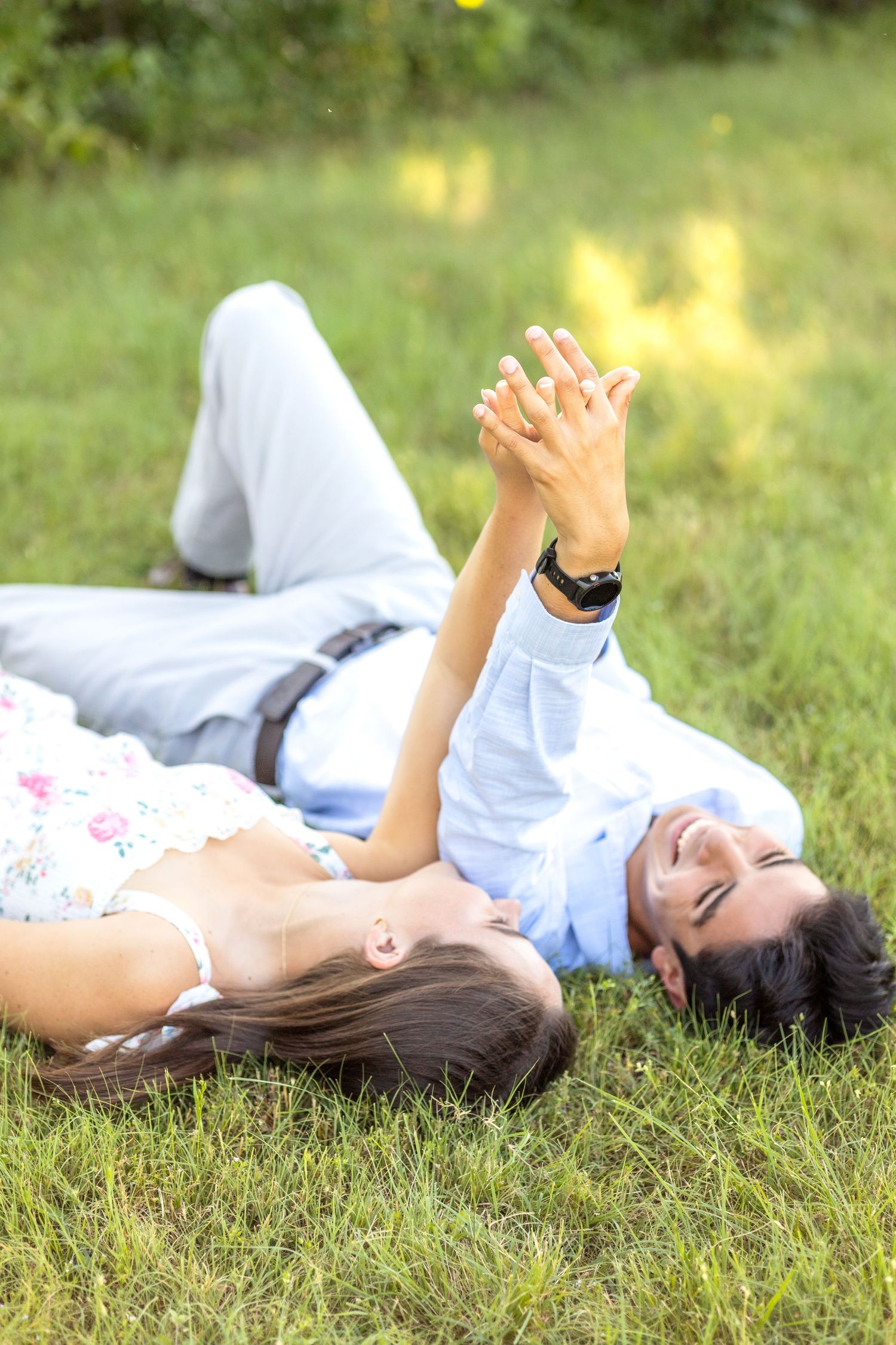 Engaged couple laying on their backs in the grass and holding hands at engagement photo session at White Rock Lake in Dallas