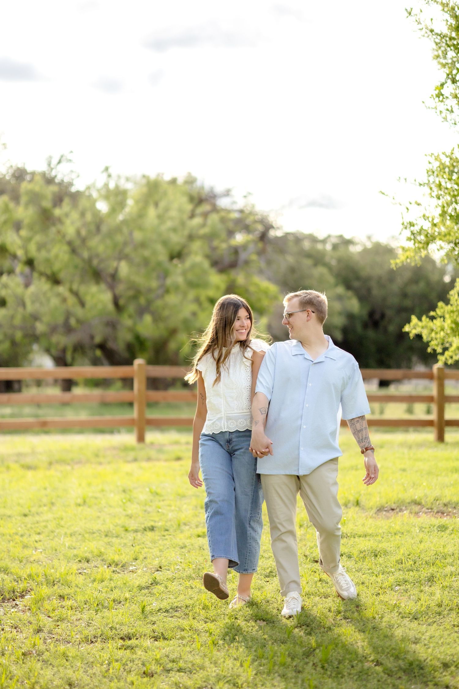 Glowy golden hour image of married couple walking hand-in-hand through a field and bumping hips in Abilene, TX couple's photo session