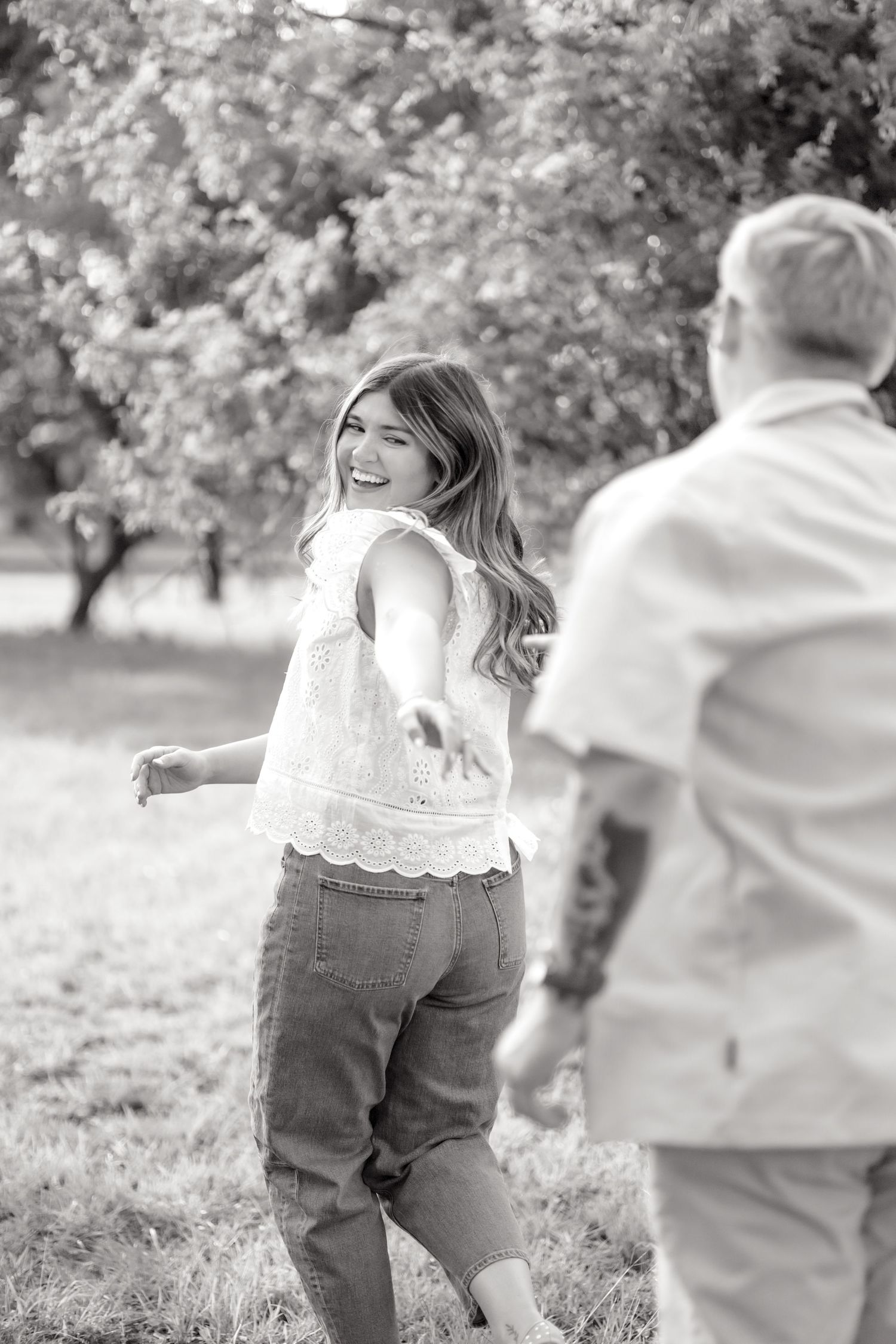 Black and white image of a wife running with her husband while she reaches her hand back for him during couple's photo session