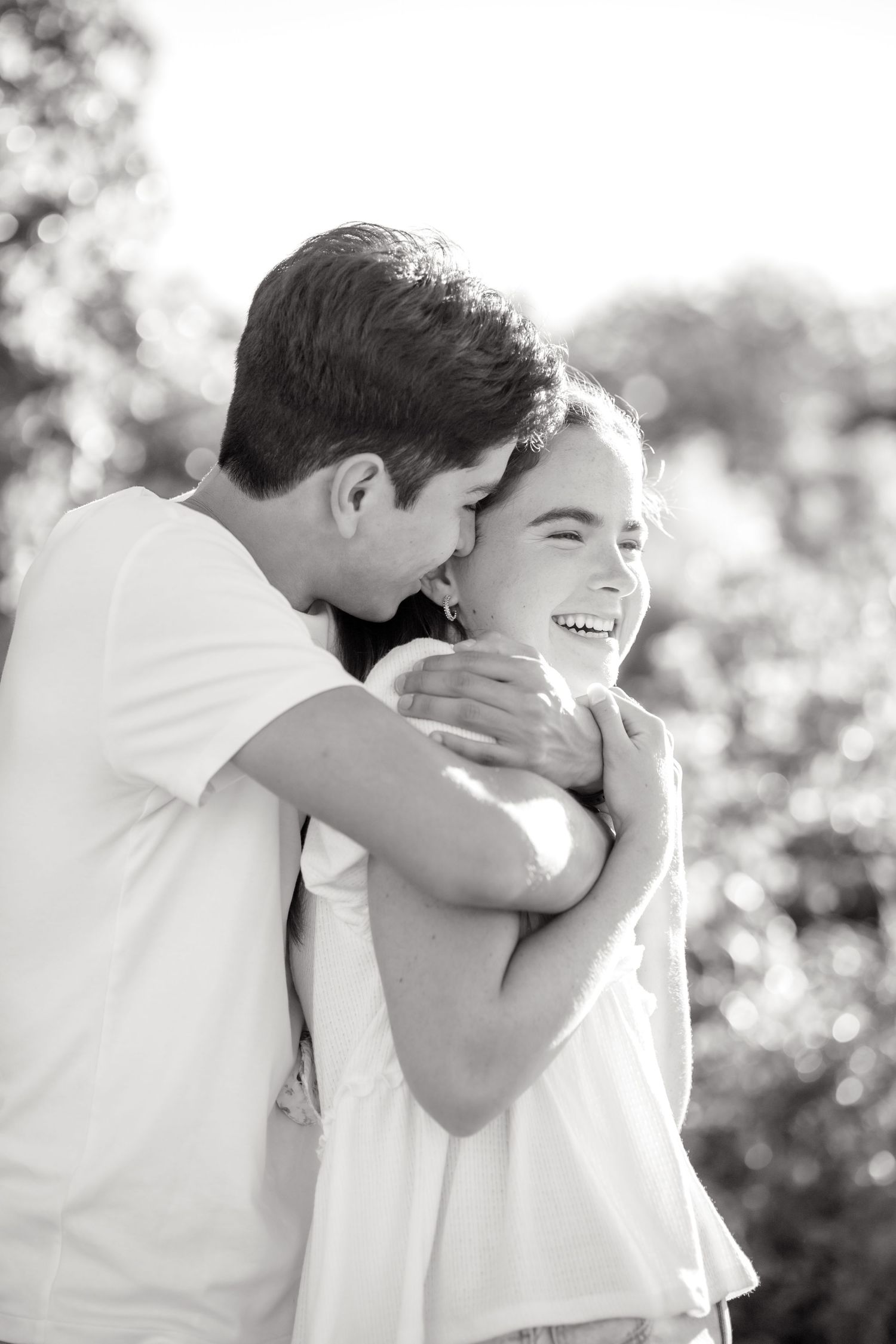 Dallas engaged couple wrapped up in a hug with groom-to-be whispering in his fiancé's ear at engagement photo session