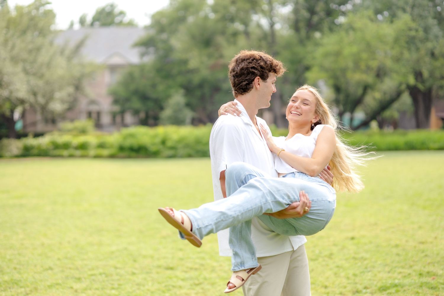 Engaged man scooping up his fiancé and spinning her around in the field at Flippen Park in Dallas, TX during engagement session