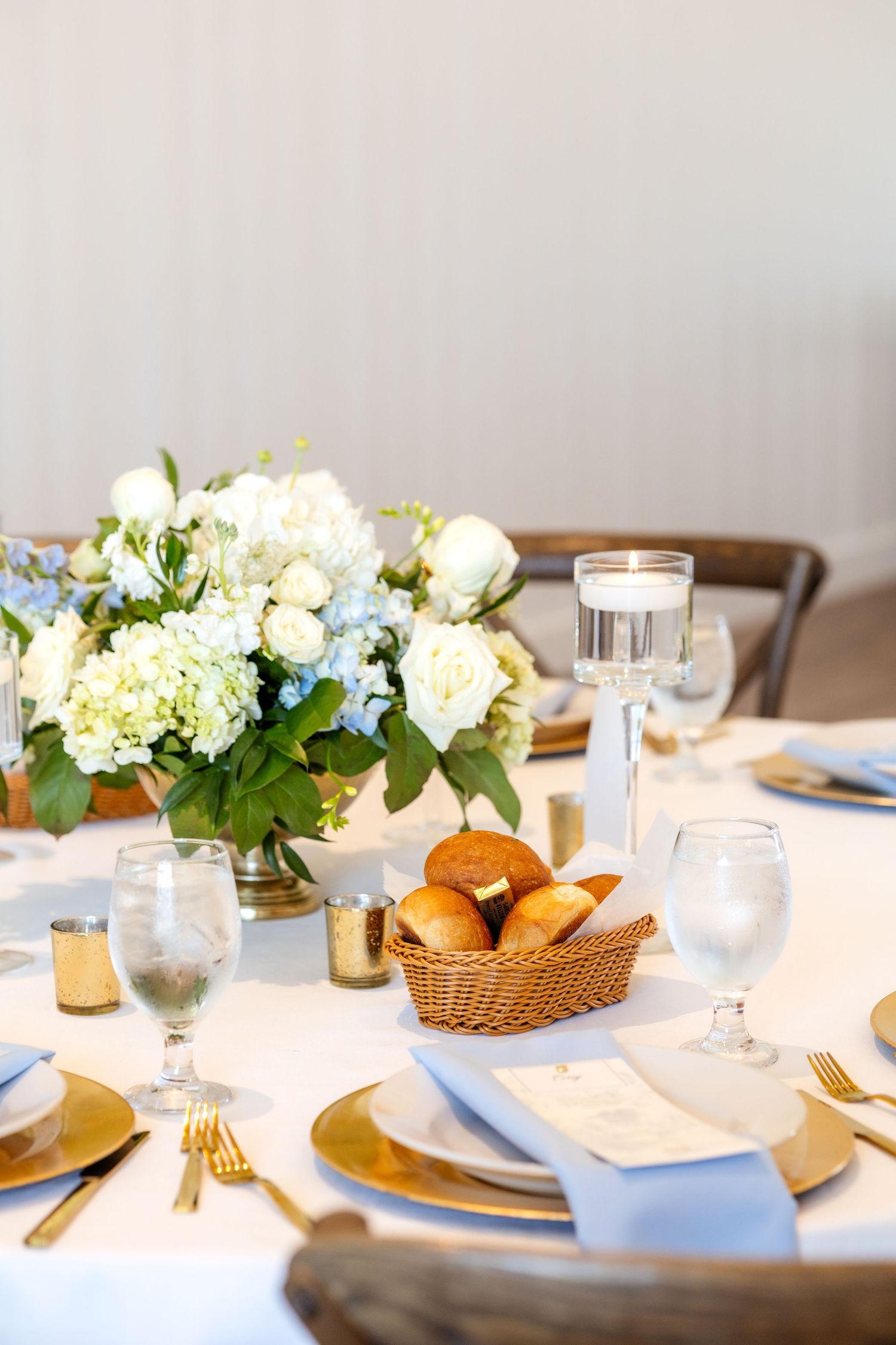 Spring wedding reception table with beautiful blue and white floral centerpieces and gold dinnerware