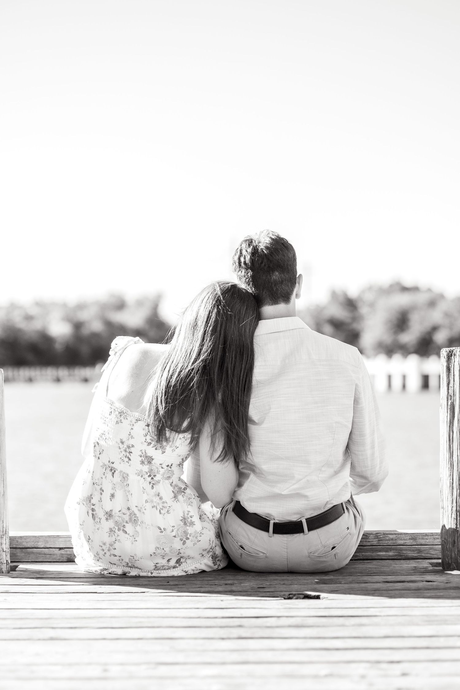 Engaged couple sitting on the dock facing away looking out at the lake at White Rock Lake in Dallas during engagement photo session
