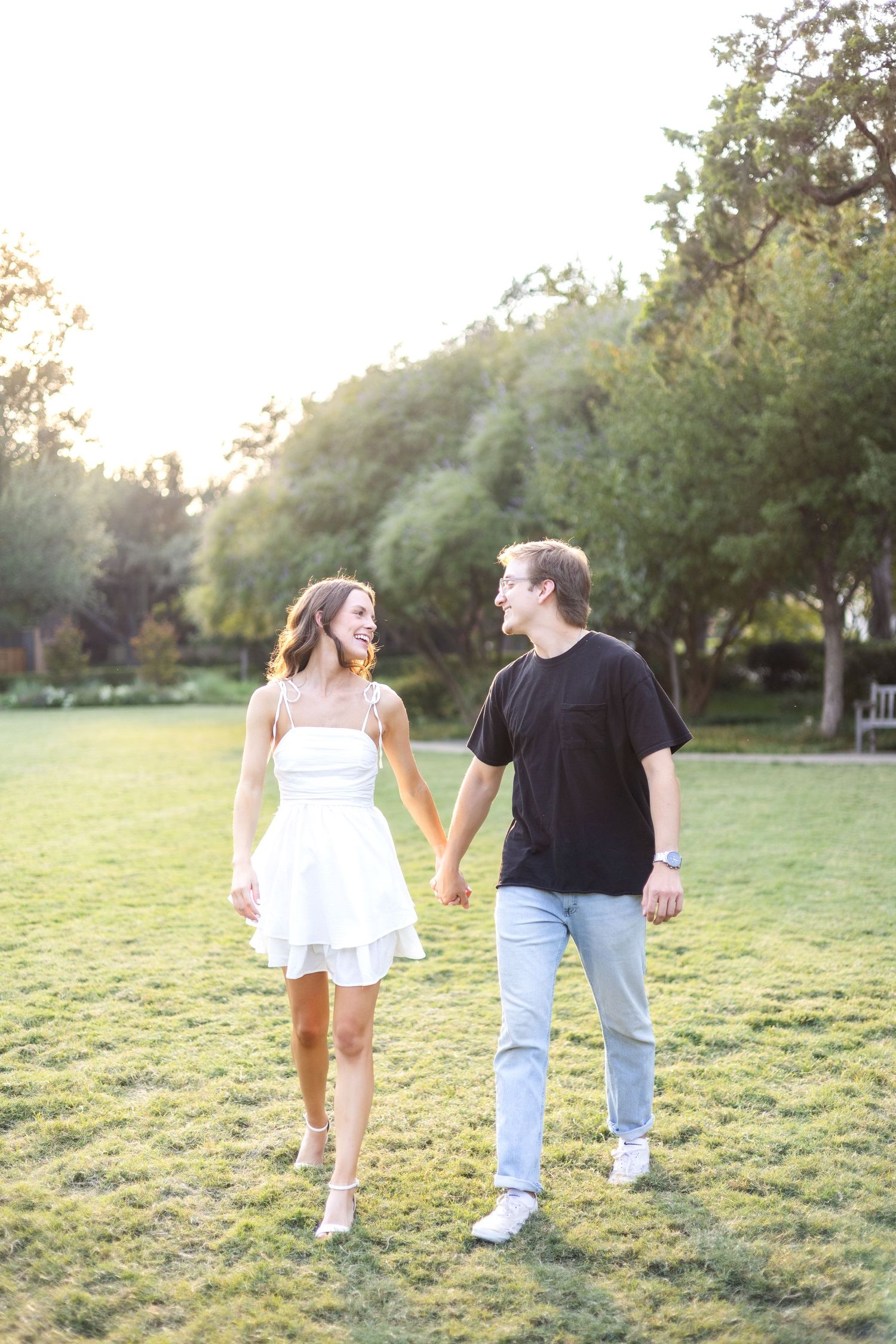 Engaged couple walking holding hands and smiling at one another in a beautiful field at Flippen Park in Dallas, TX during engagement session