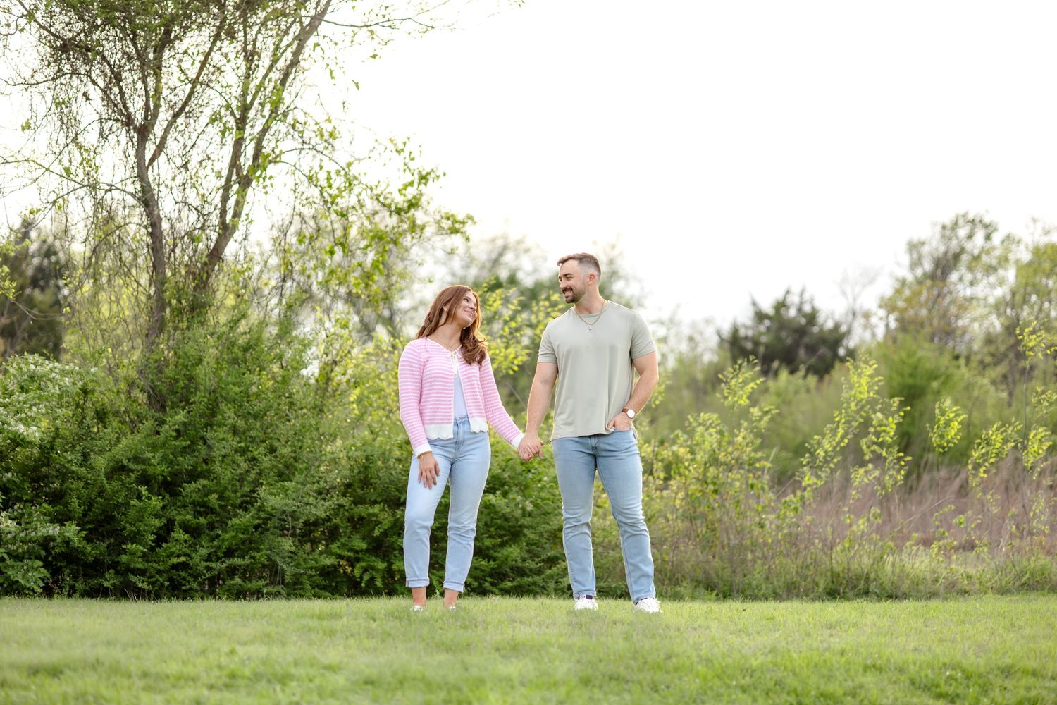 Beautiful and dreamy engagement photo of a couple holding hands and looking at one another in a field at White Rock Lake in Dallas, Texas