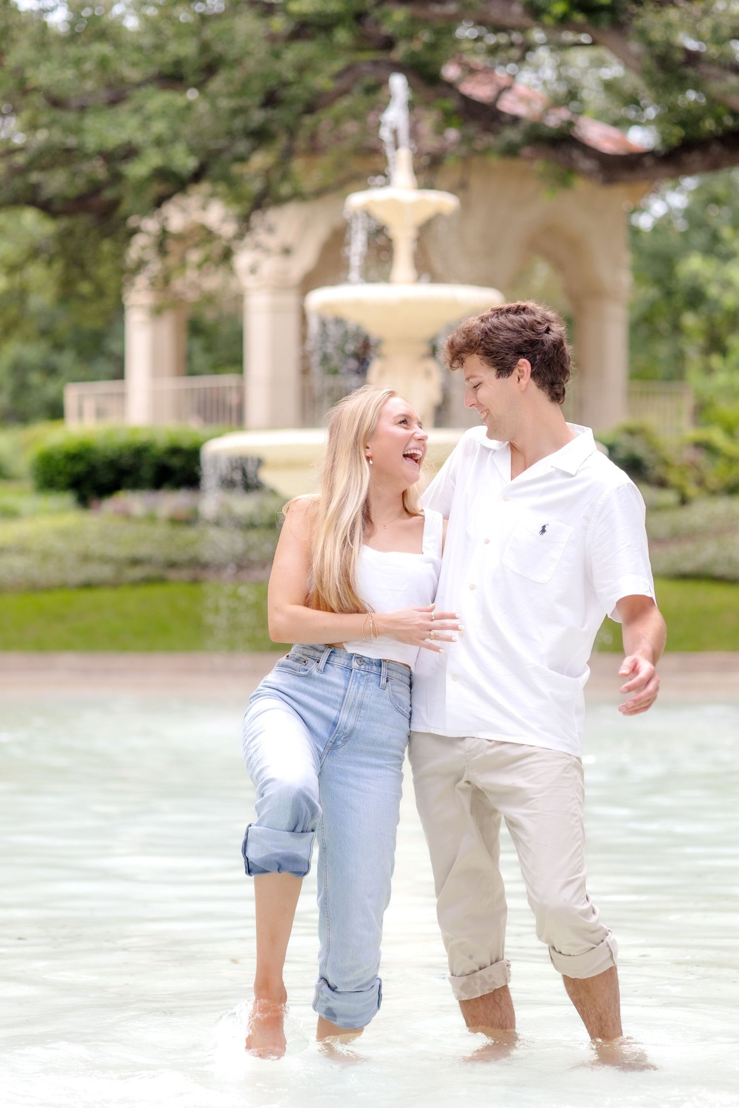Engaged couple standing and splashing around in the fountain at Flippen Park in Dallas, TX during engagement photo session