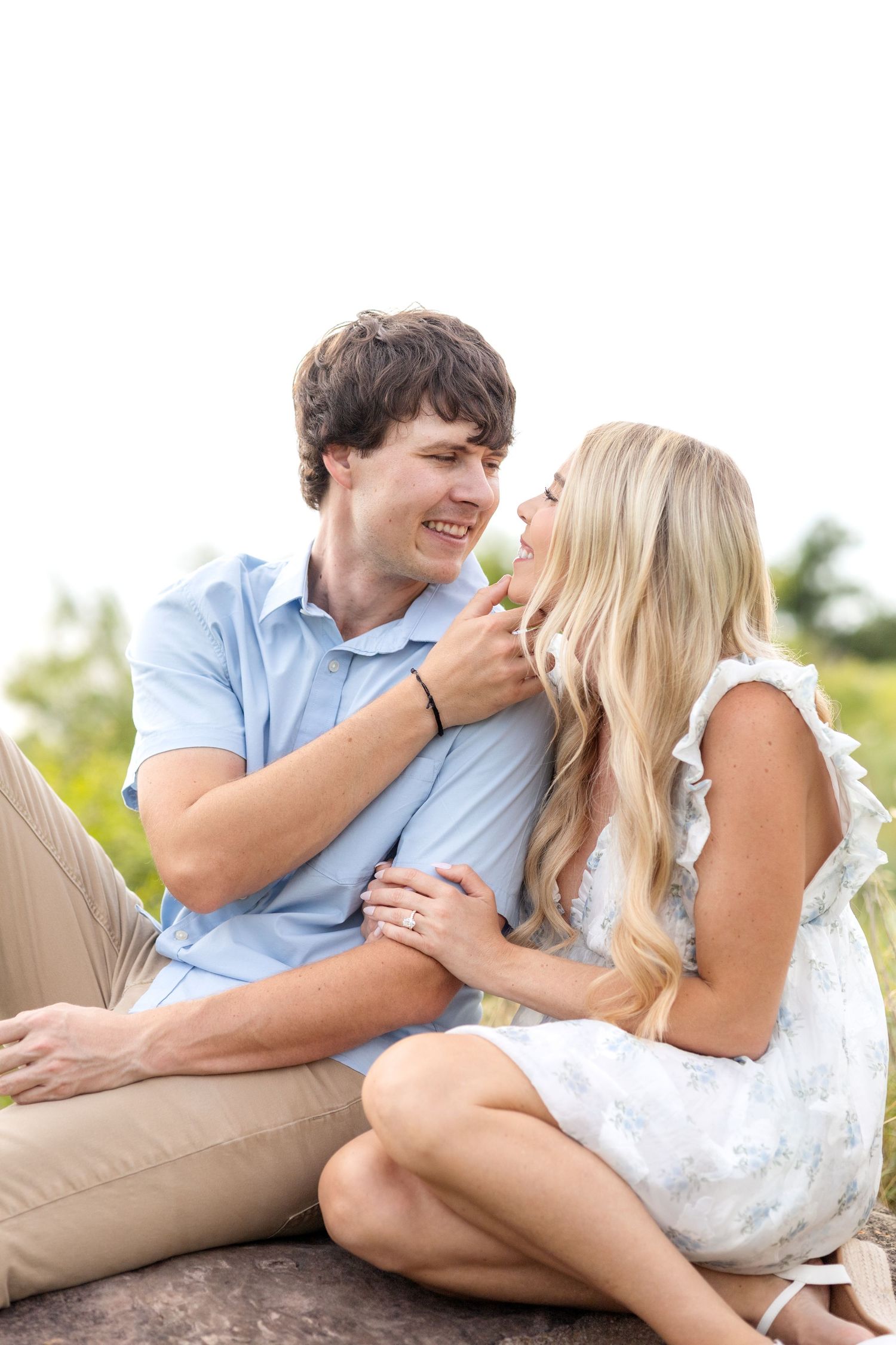 Engaged couple sitting side by side as he pulls his fiancé in close for a kiss during Texas engagement photo session