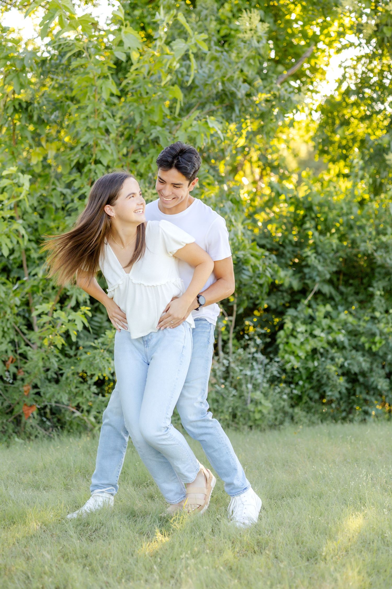 Engaged couple playing around with one another in the field at White Rock Lake during their engagement photo session in Dallas