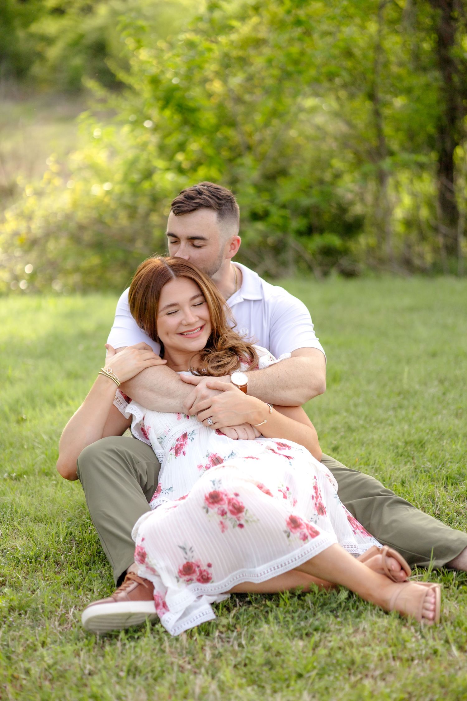 engaged couple sitting in a field and kissing the forehead at White Rock Lake in Dallas, Texas during their engagement photo session