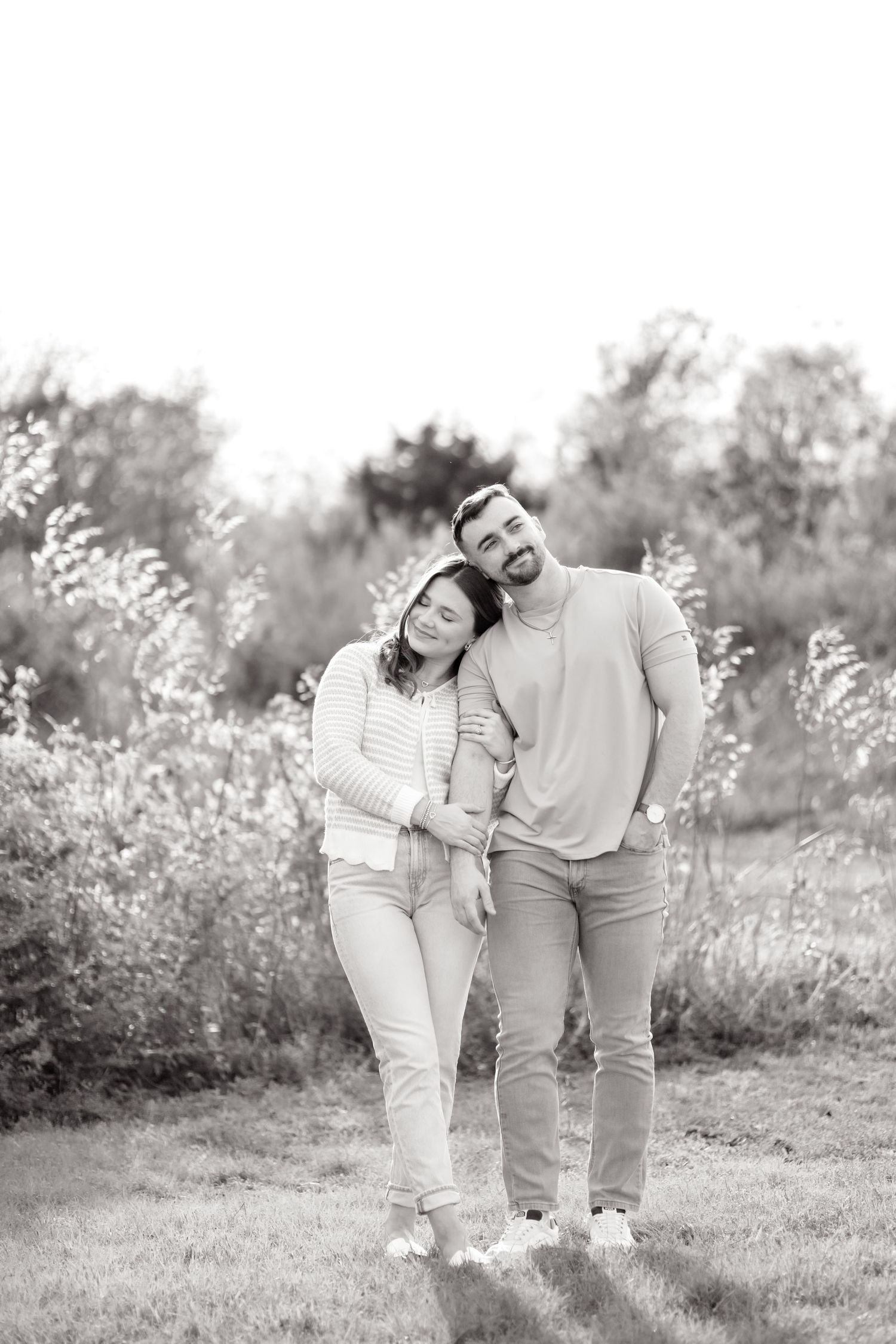 Married couple standing side by side and resting her head on his shoulder, looking in opposite directions