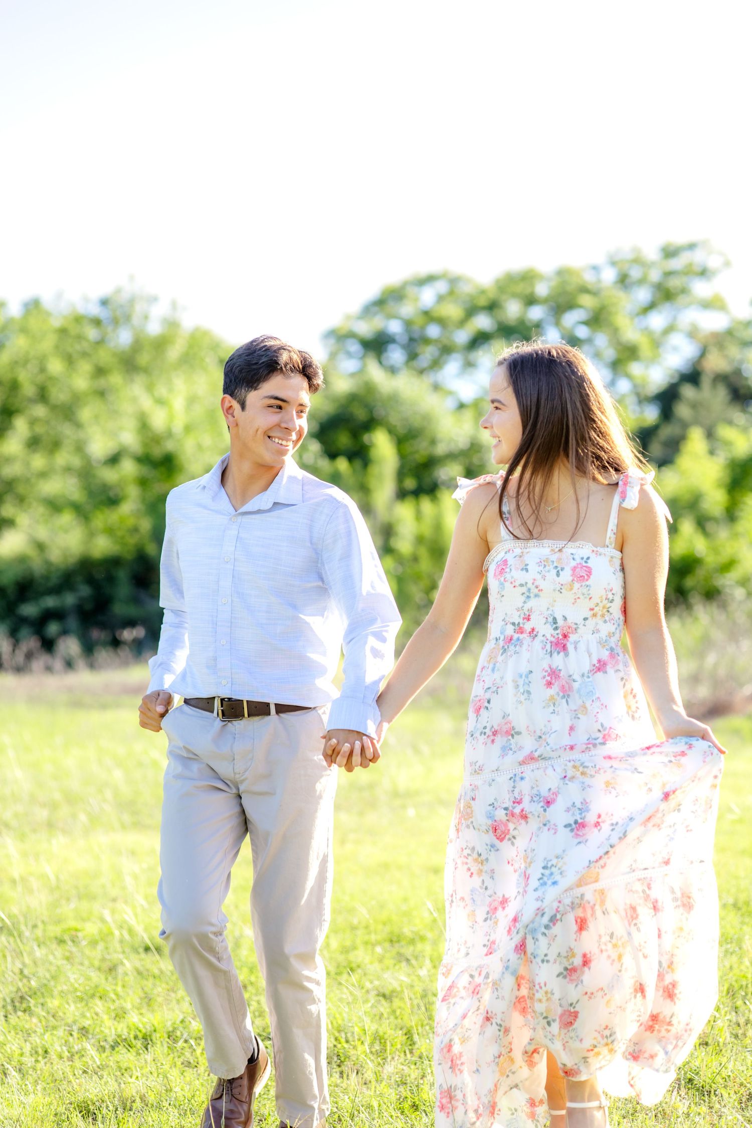 Engaged couple running hand-in-hand and laughing in a field at White Rock Lake in Dallas during their engagement session