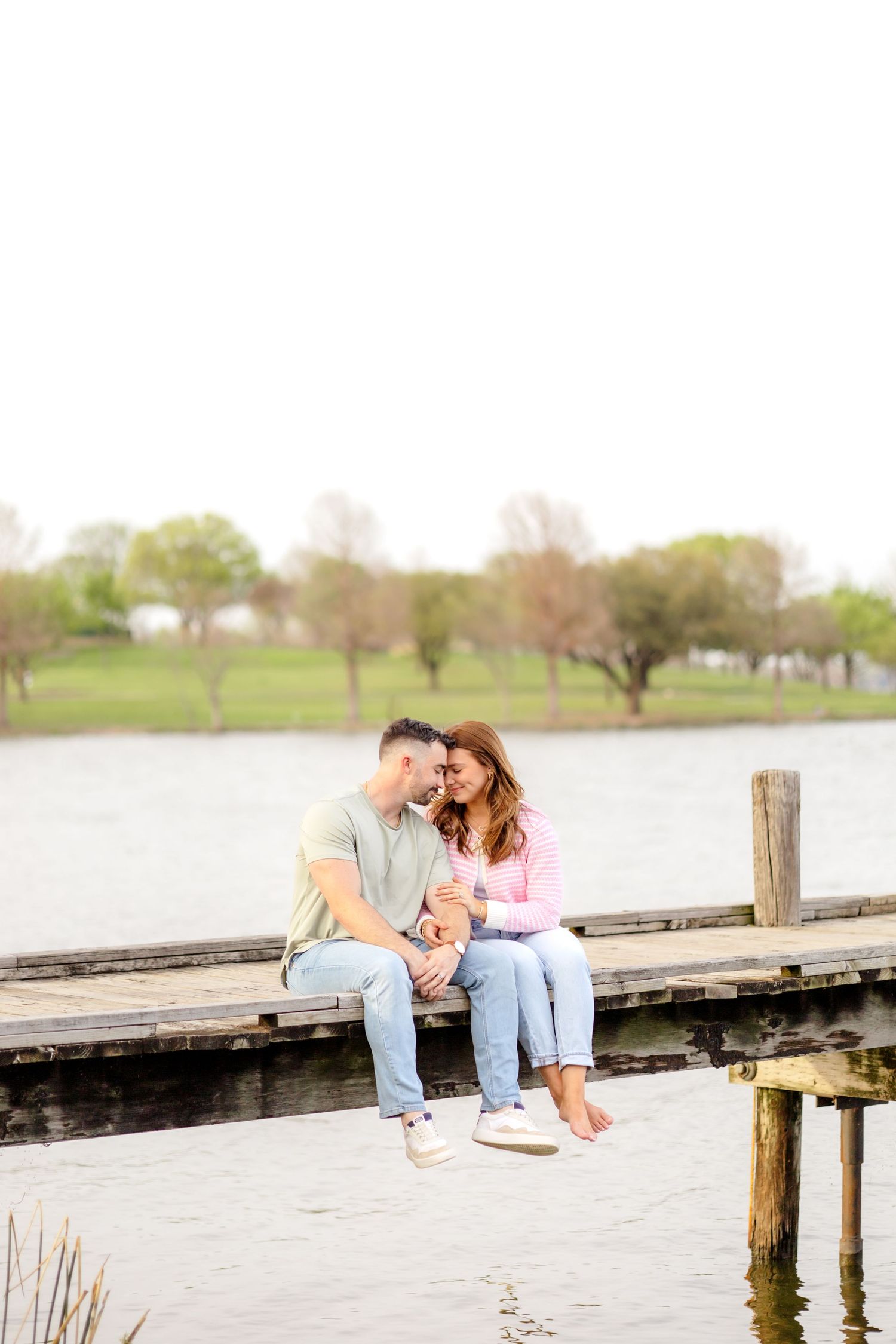 Married couple sitting on the dock at White Rock Lake and snuggling in close to one another
