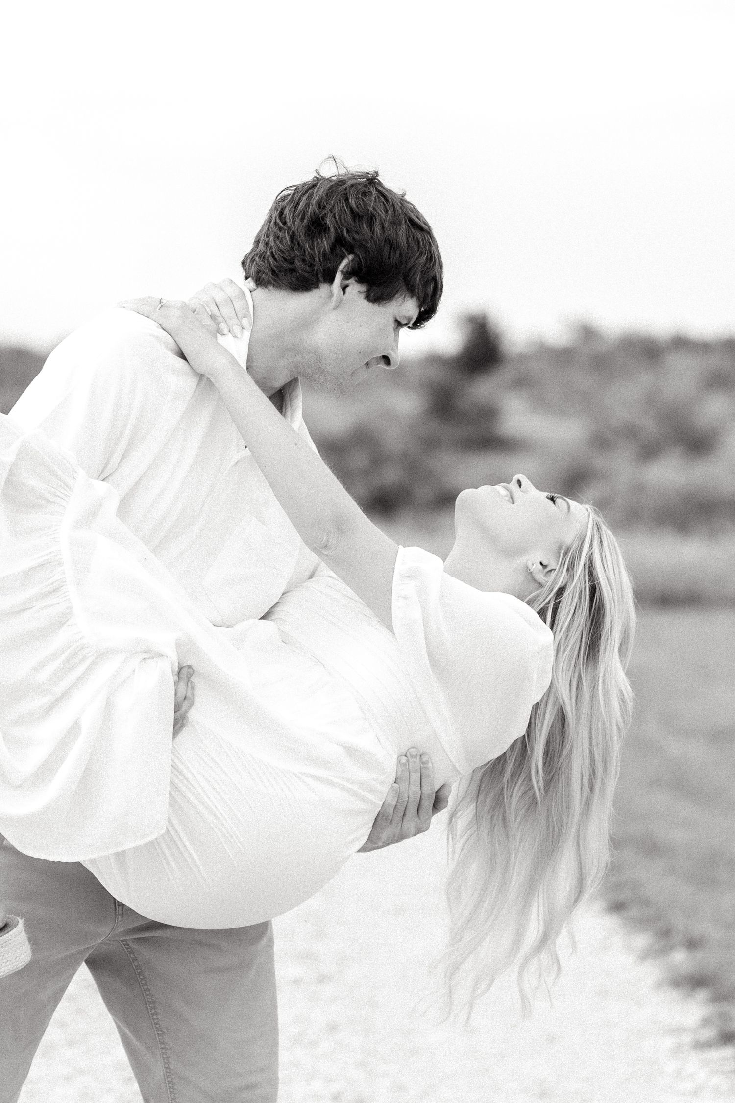 Black and white image of engaged man dipping his fiancé back as she leans her head back to make her hair fall at Texas engagement session