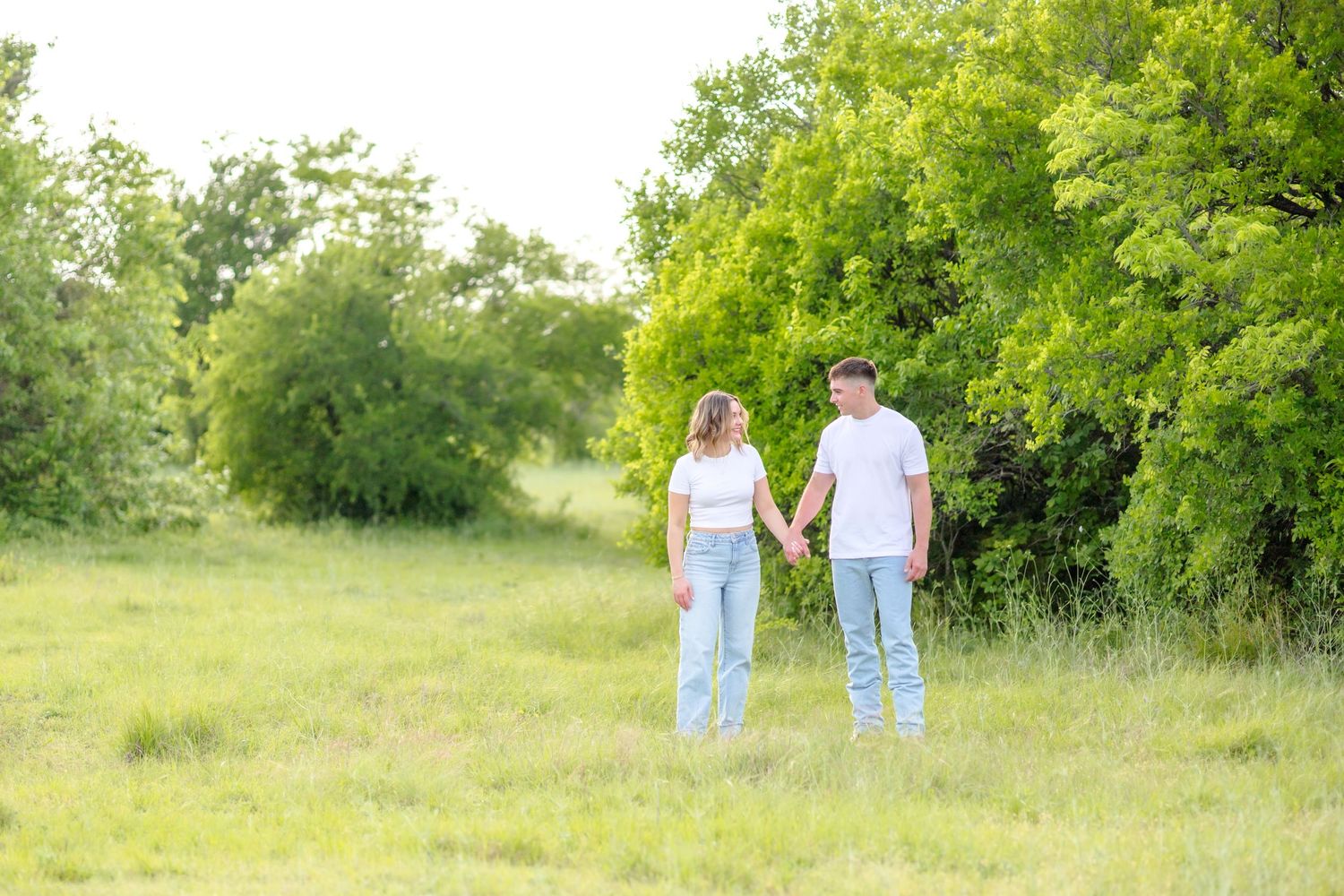 Engaged couple holding hands in a beautiful field at engagement photo session at Arbor Hills Nature Preserve in Plano, TX