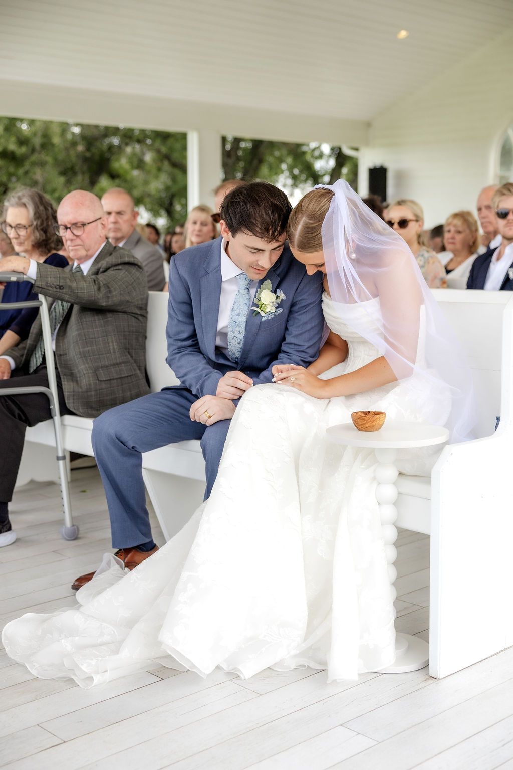 Bride and groom holding hands and praying during communion inside the open-air chapel at Chandelier Farms