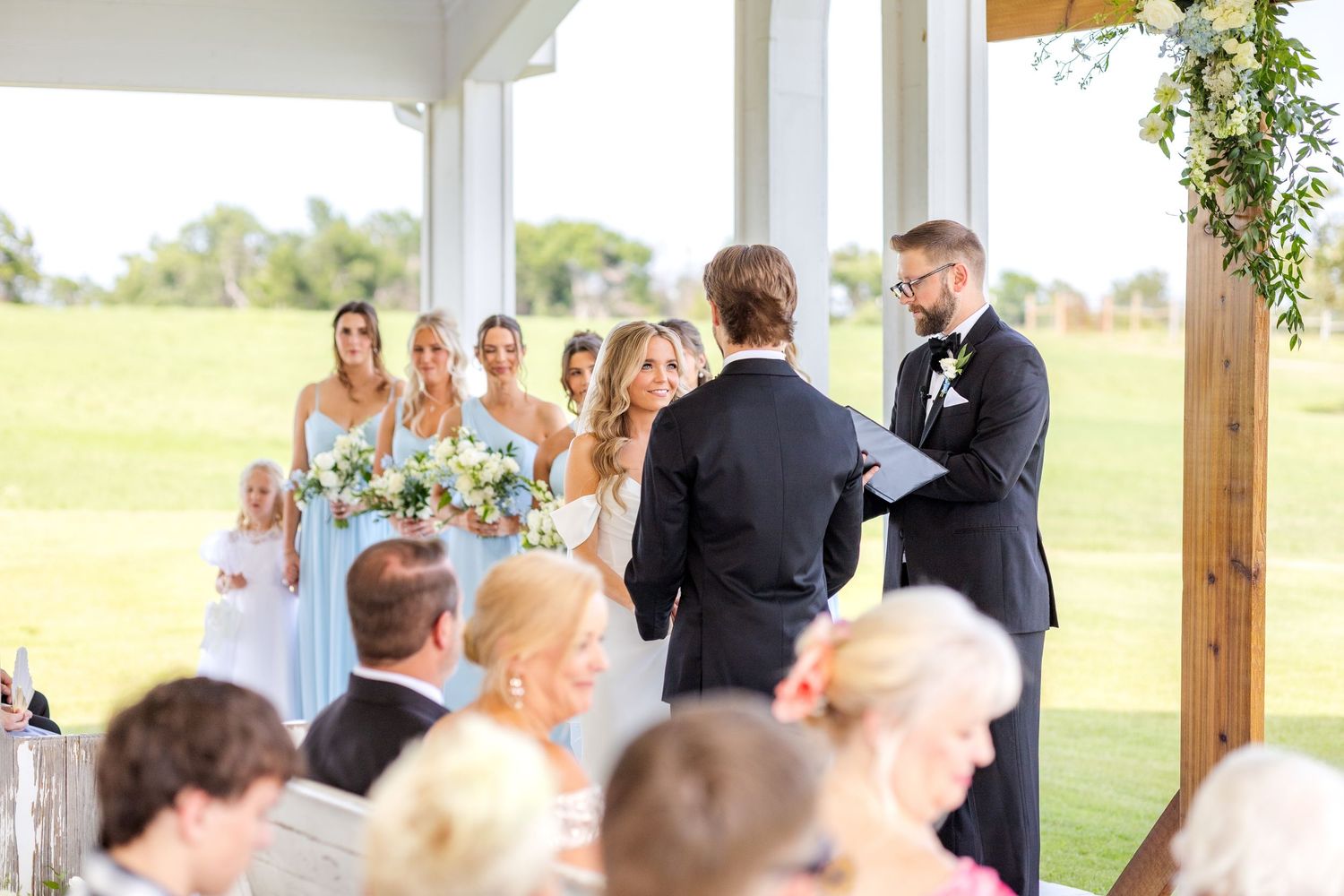 Spring Dallas wedding ceremony at Chandelier Farms with bride smiling big at her soon to be husband while reciting wedding vows