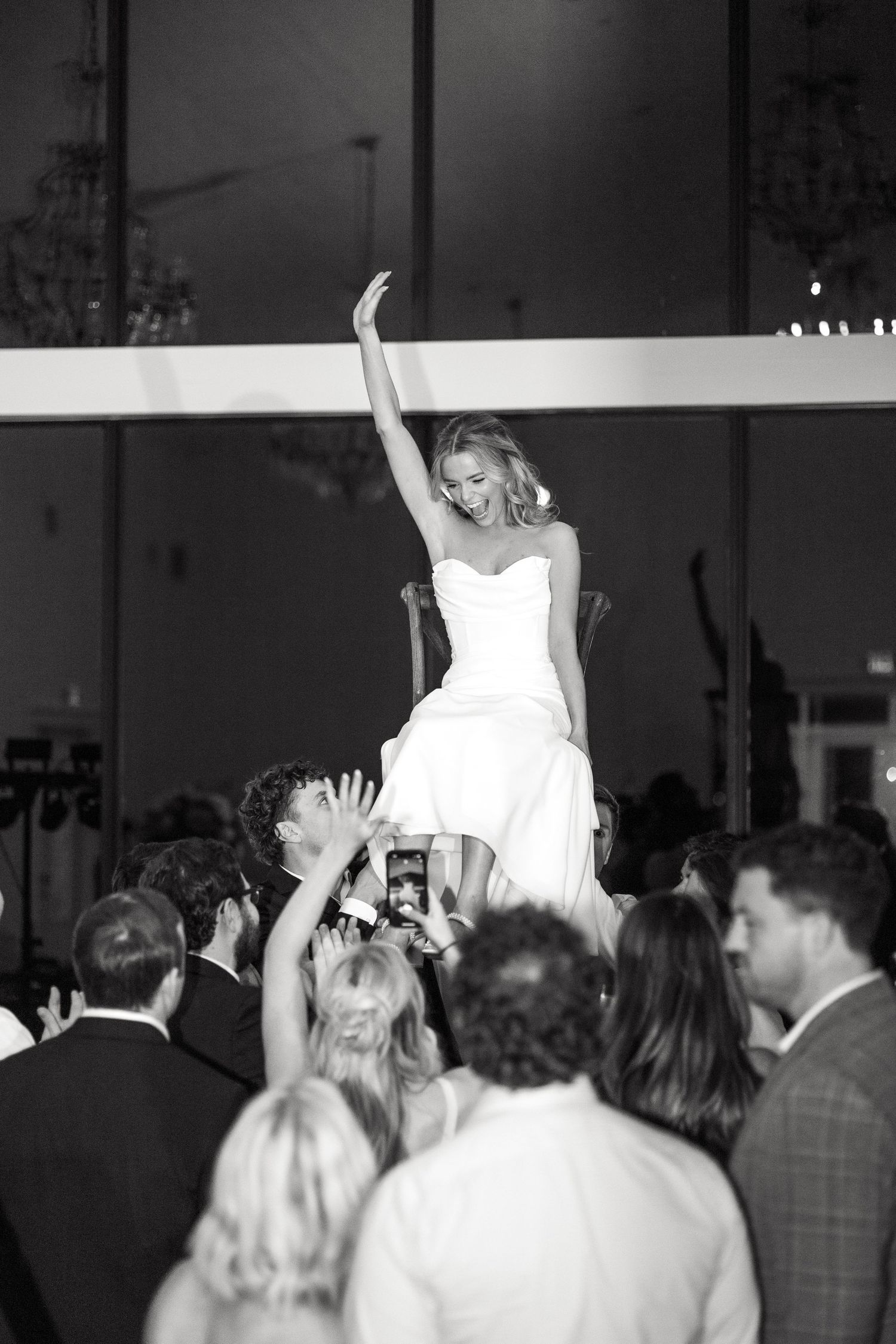 Bride sitting on a chair that guests lift up into the air as the bride throws her hands in the air during Dallas wedding reception