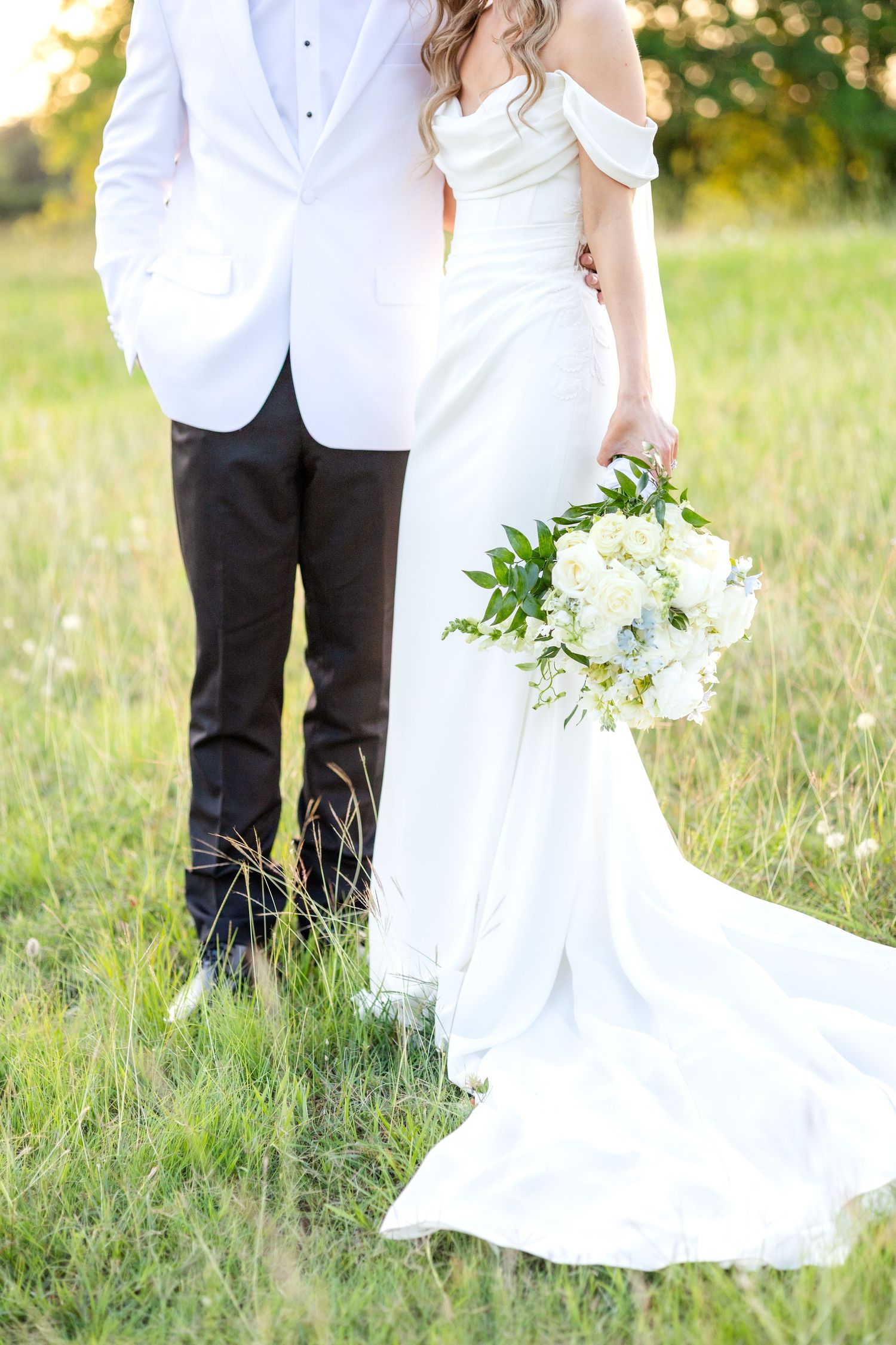 Bride and groom standing in golden field during sunset at Dallas wedding holding spring wedding flowers