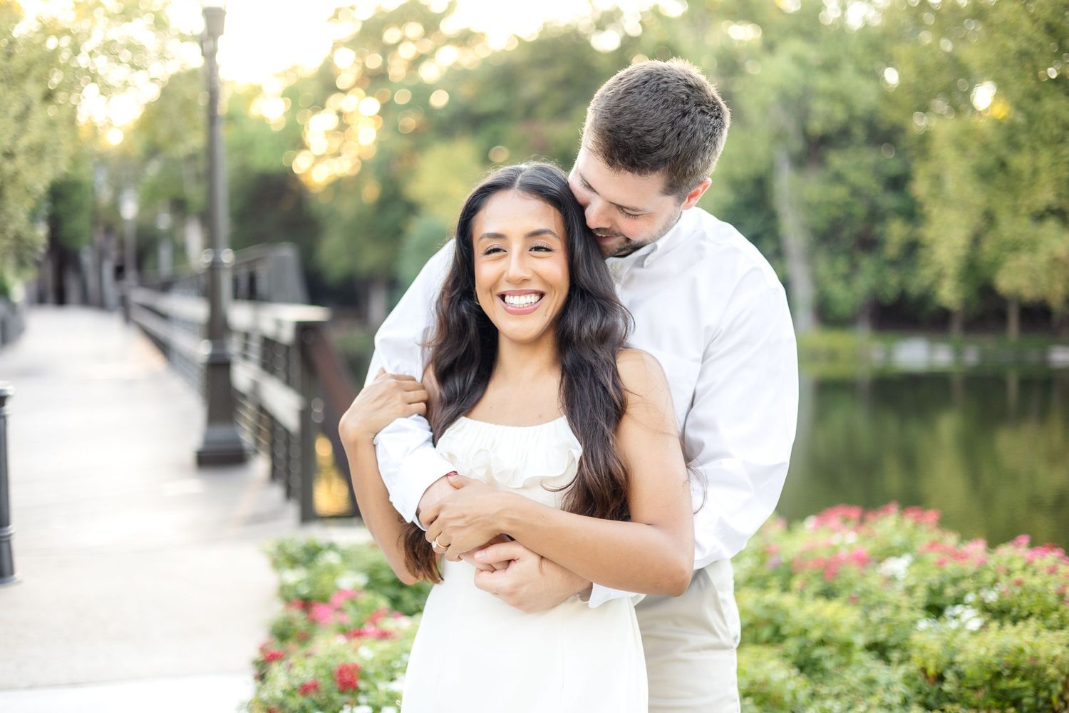 Engaged couple hugging and whispering sweetly into her ear at Lakeside Park in Dallas, TX during engagement photo session