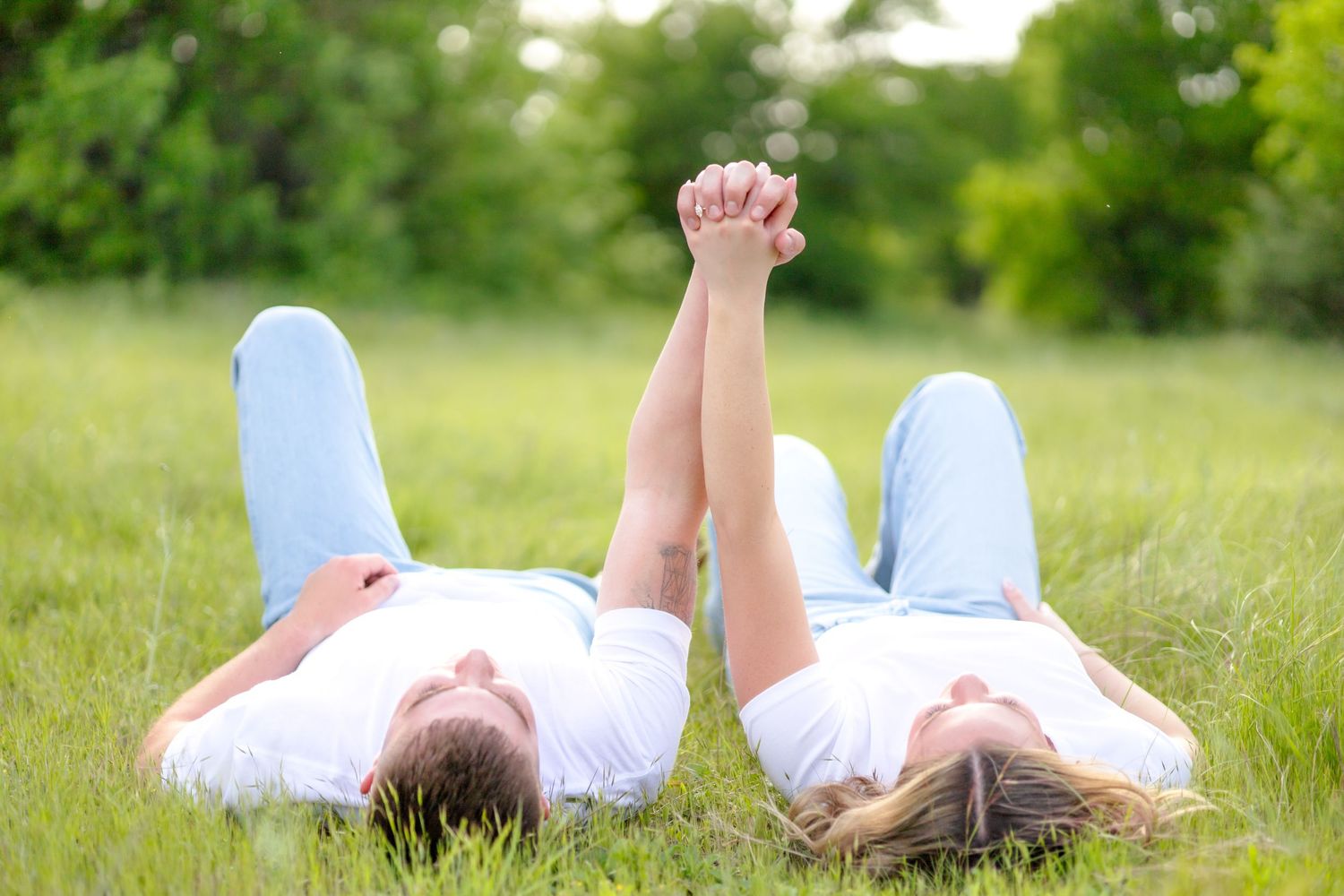 Engagement session photo of a couple laying in the grass holding hands