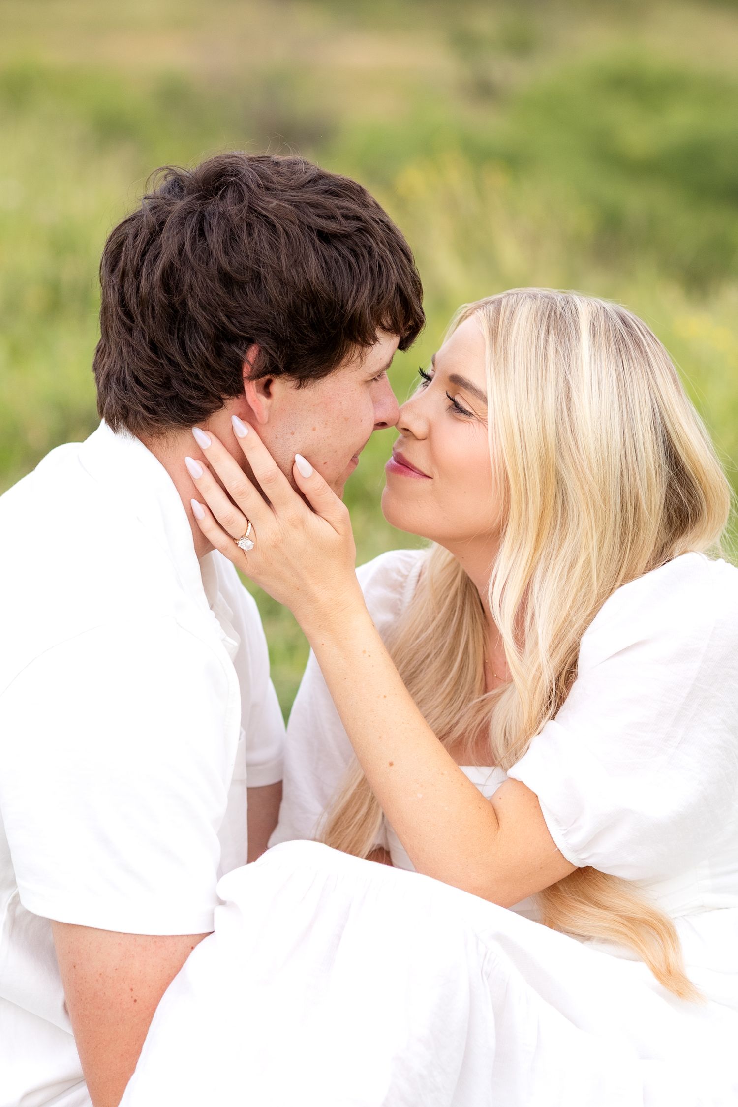 Engaged couple sitting close together in a field in Texas during engagement session and going nose-to-nose