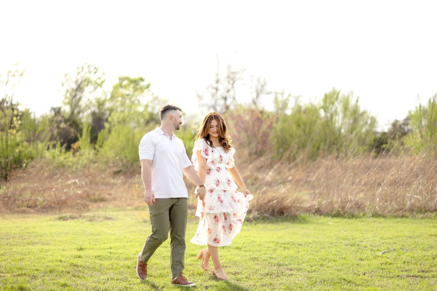 engaged couple walking in a field in Dallas at White Rock Lake during engagement photo session