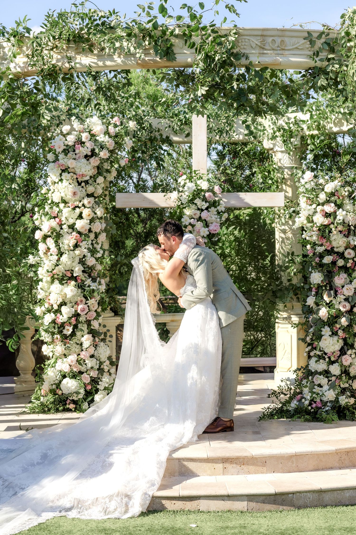 Bride and groom first kiss at D'Vine Grace Vineyard with lush green and pink florals
