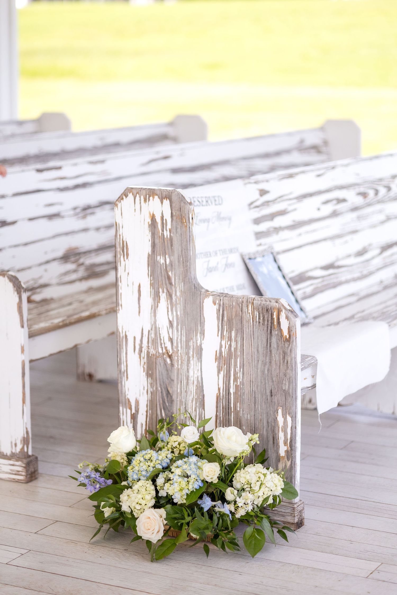Wedding ceremony florals on the ground resting next to a chapel pew at Dallas wedding at Chandelier Farms