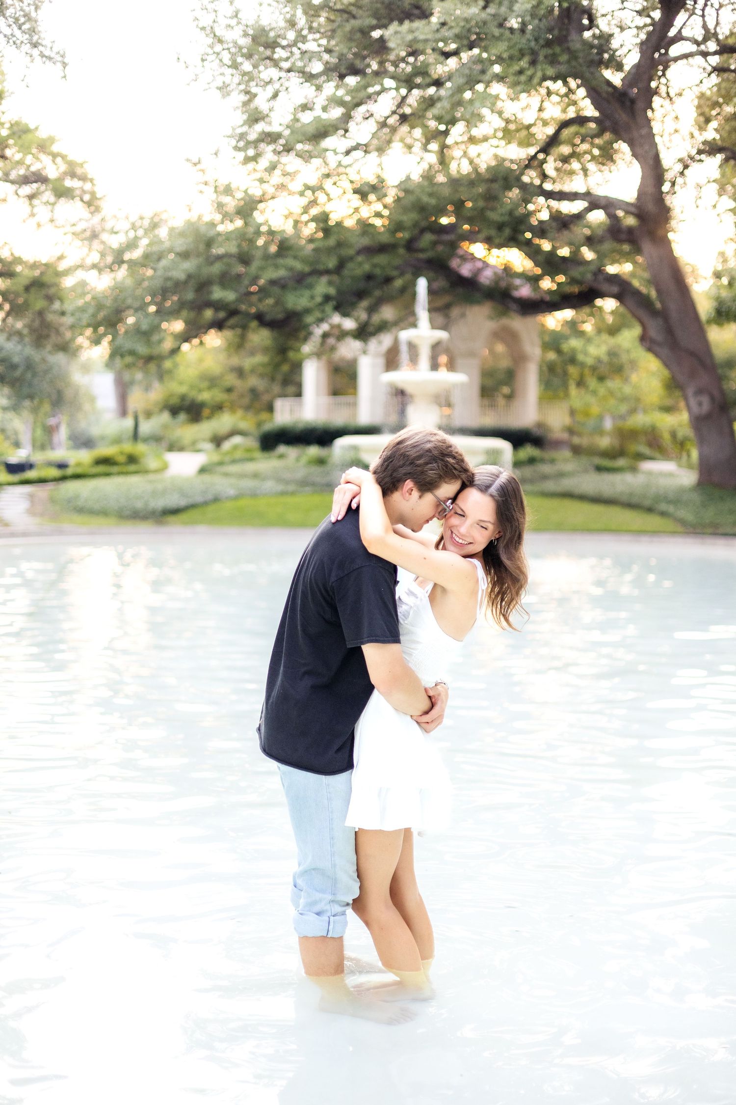 Engaged couple kissing on the cheek in a beautiful fountain at Flippen Park in Dallas, TX during engagement session