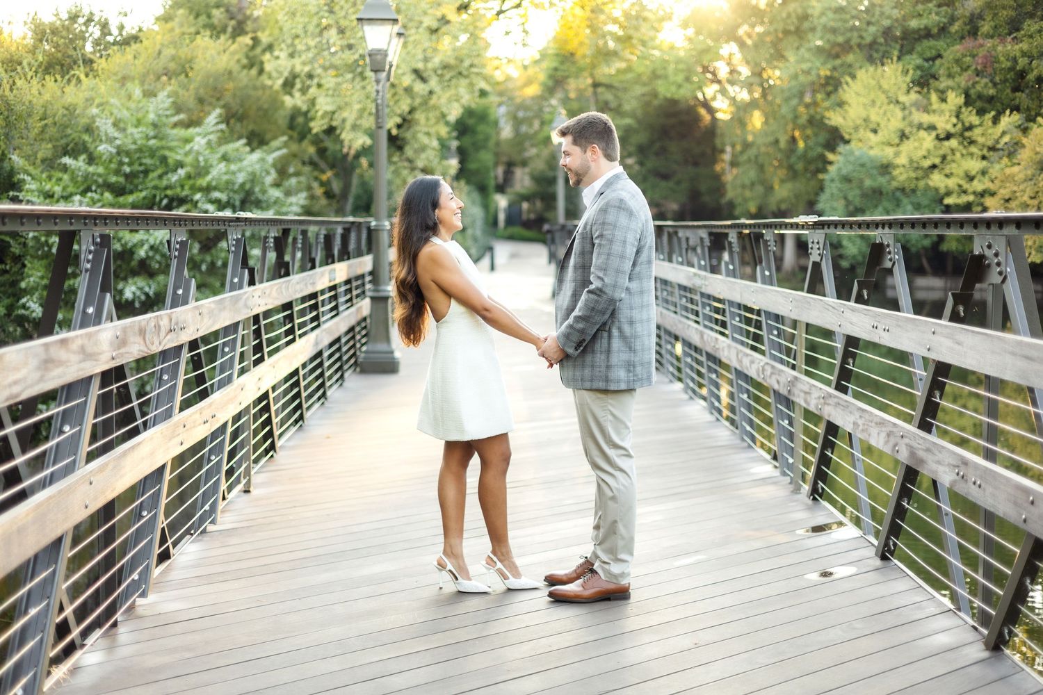 Engaged couple holding hands and facing each other on bridge at Lakeside Park in Dallas, Texas during romantic engagement photo session