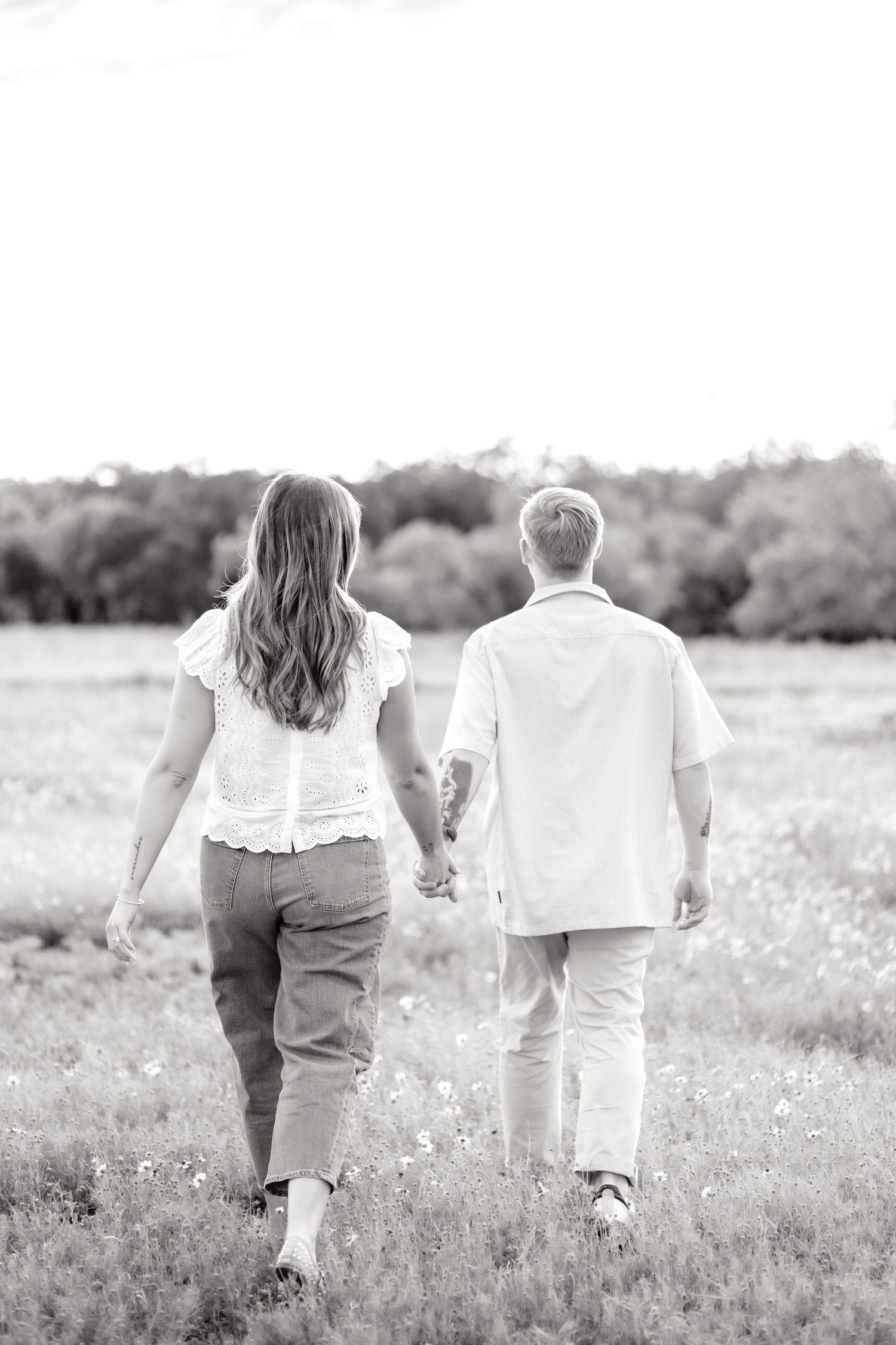 black and white image of a couple walking hand in hand through a field of flowers