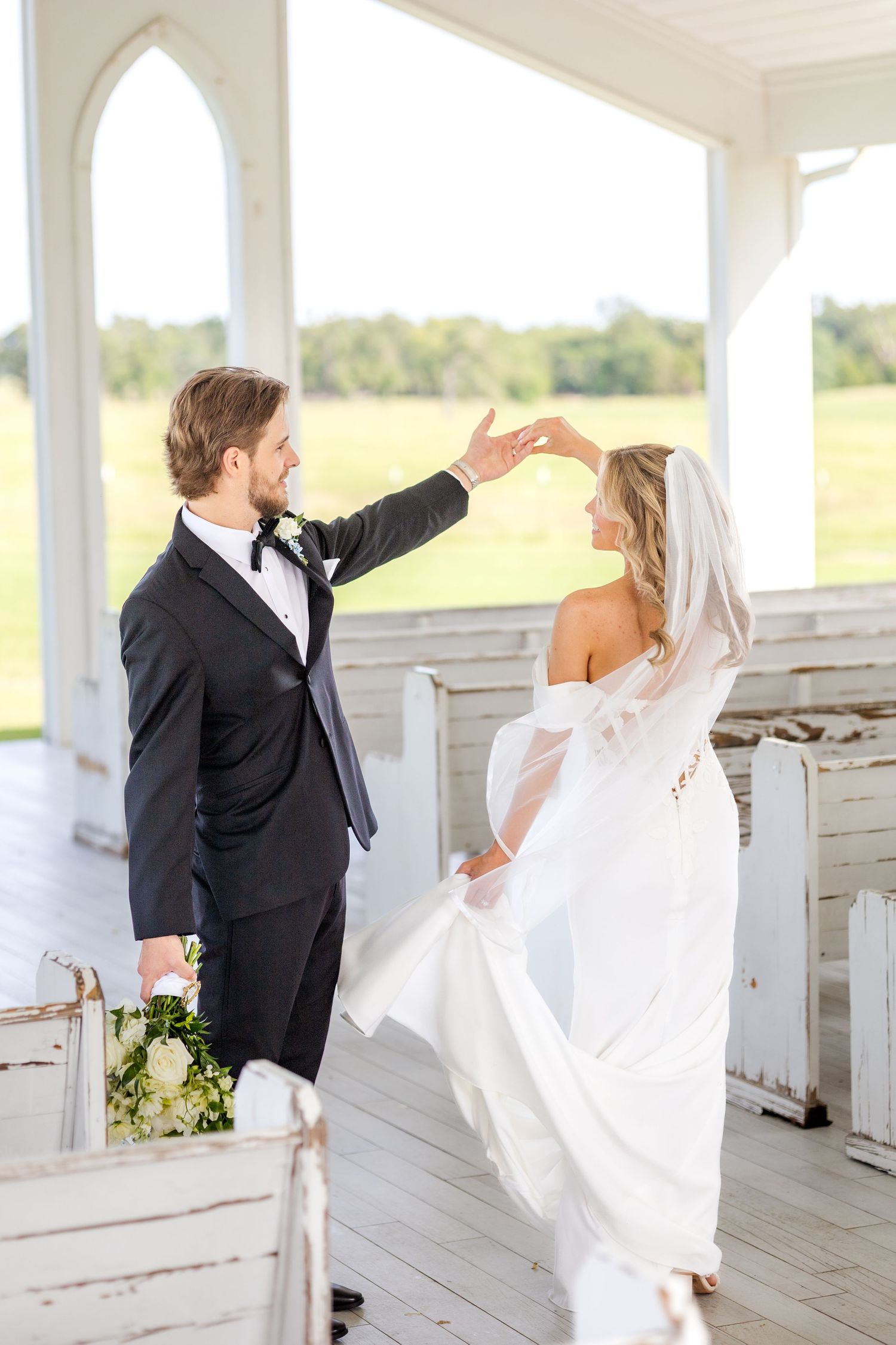 Groom spinning his bride like a princess inside a Dallas wedding chapel while holding her Spring wedding bouquet at Chandelier Farms