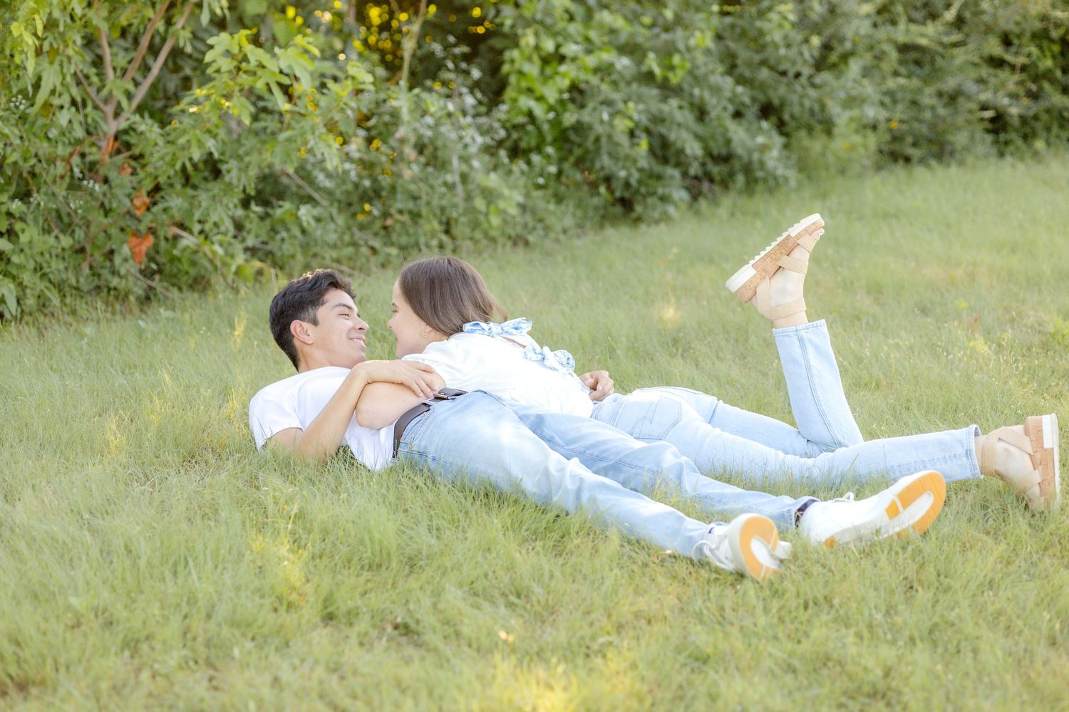 Engaged couple laying down in the grass with bride-to-be resting on her fiancé's chest and kicking her legs at engagement photo session