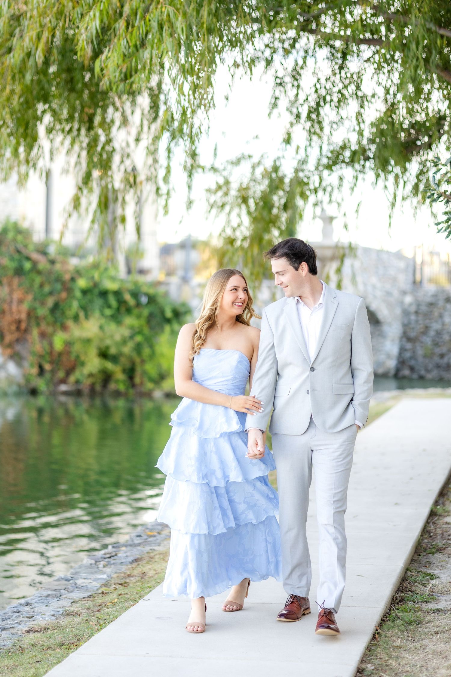 Engaged couple walking hand in hand under a beautiful tree at Adriatica Village in McKinney during Dallas engagement session