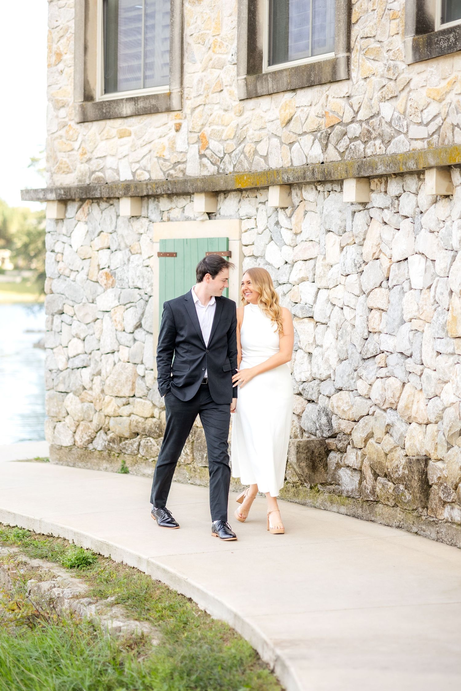 Dallas engaged couple walking holding hands in front of stone building at Adriatica Village in McKinney, TX during engagement session.