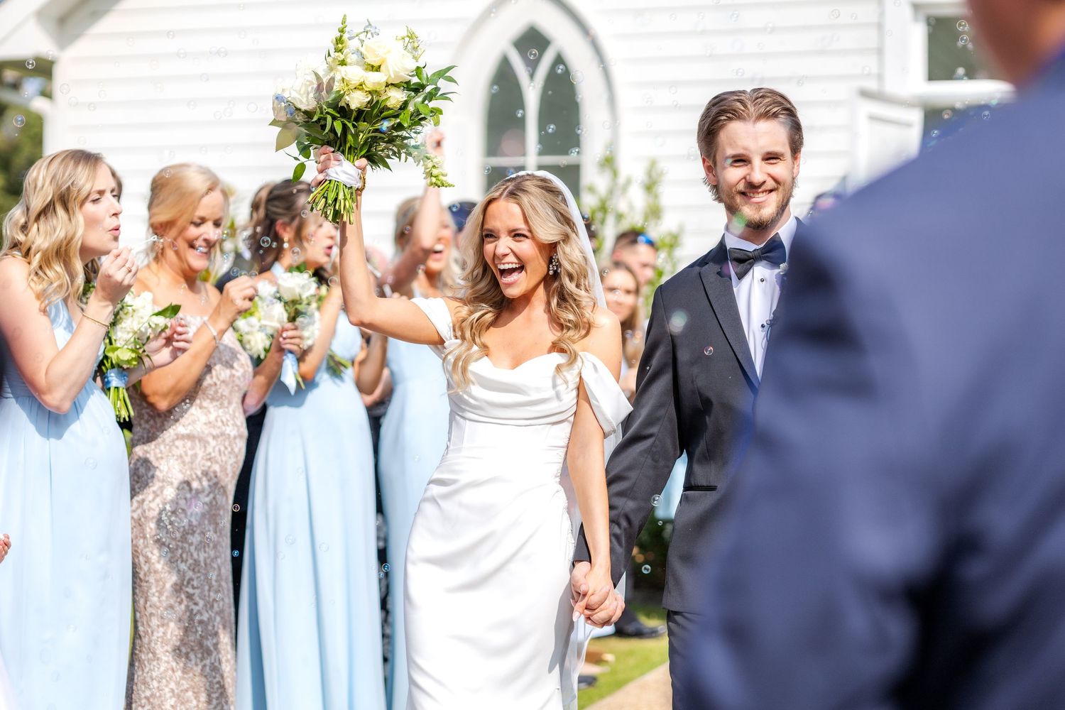 Bride and groom exiting their wedding ceremony at Chandelier Farms near Dallas, Texas as guests line up and blow bubbles toward them