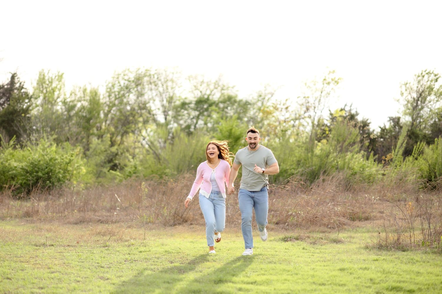 Married couple holding hands and running through a field at White Rock Lake