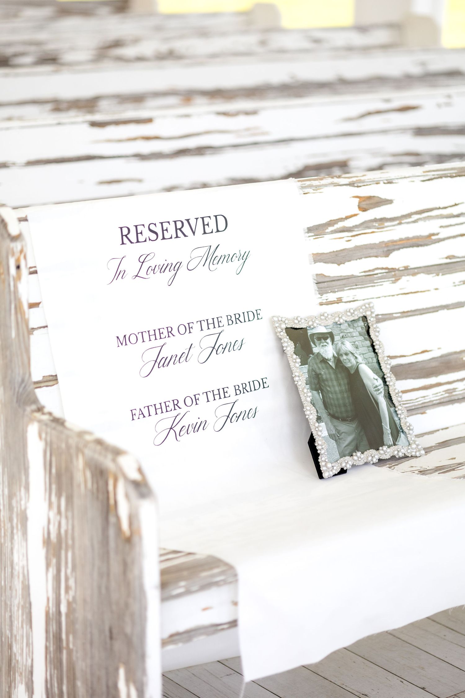 Cloth reserved sign for bride's parents who have passed away and a photo of the bride's parents on wedding chapel pew at Chandelier Farms