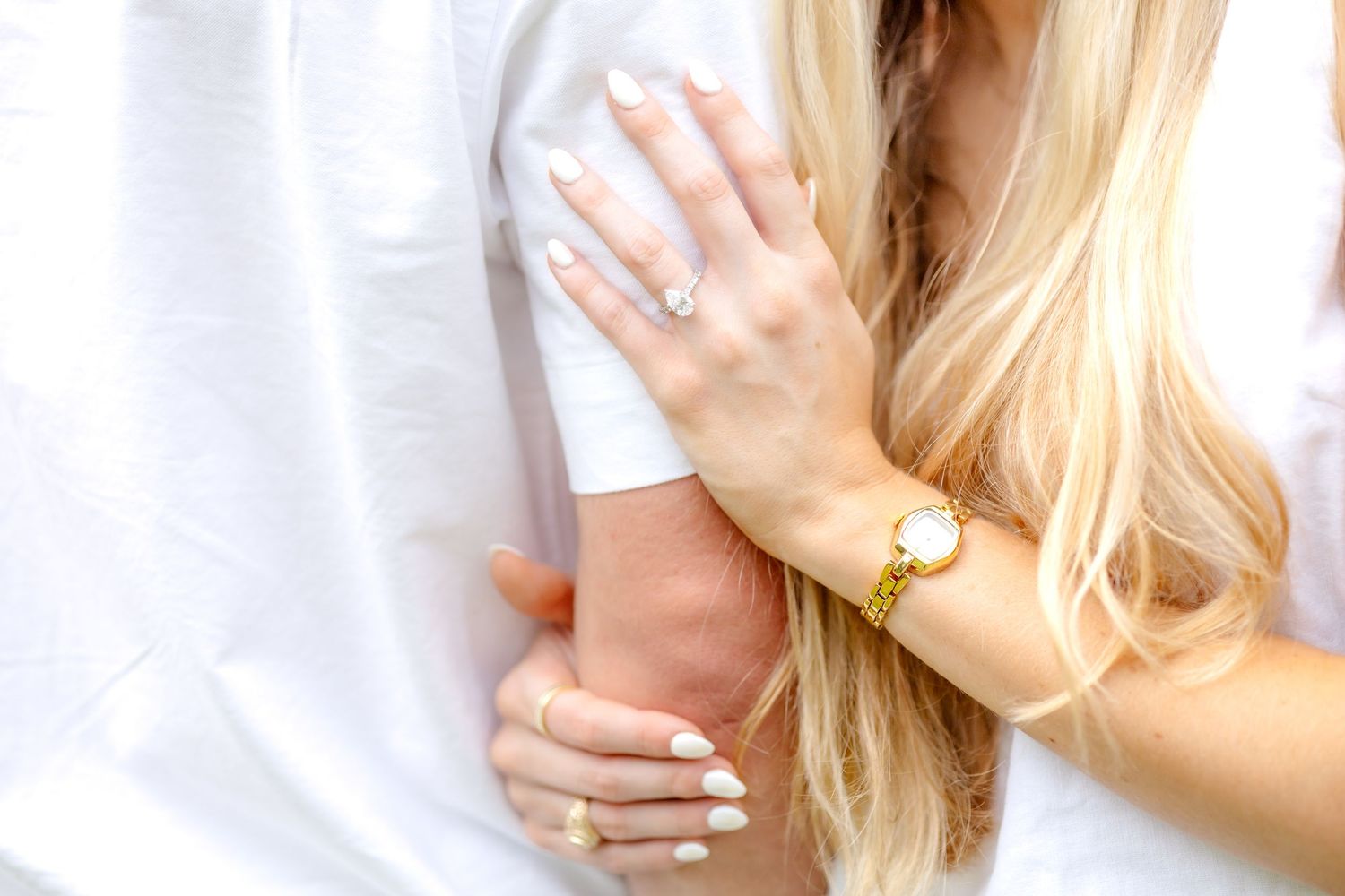 Detail image of an engaged woman's engagement ring resting on her fiancé's arm
