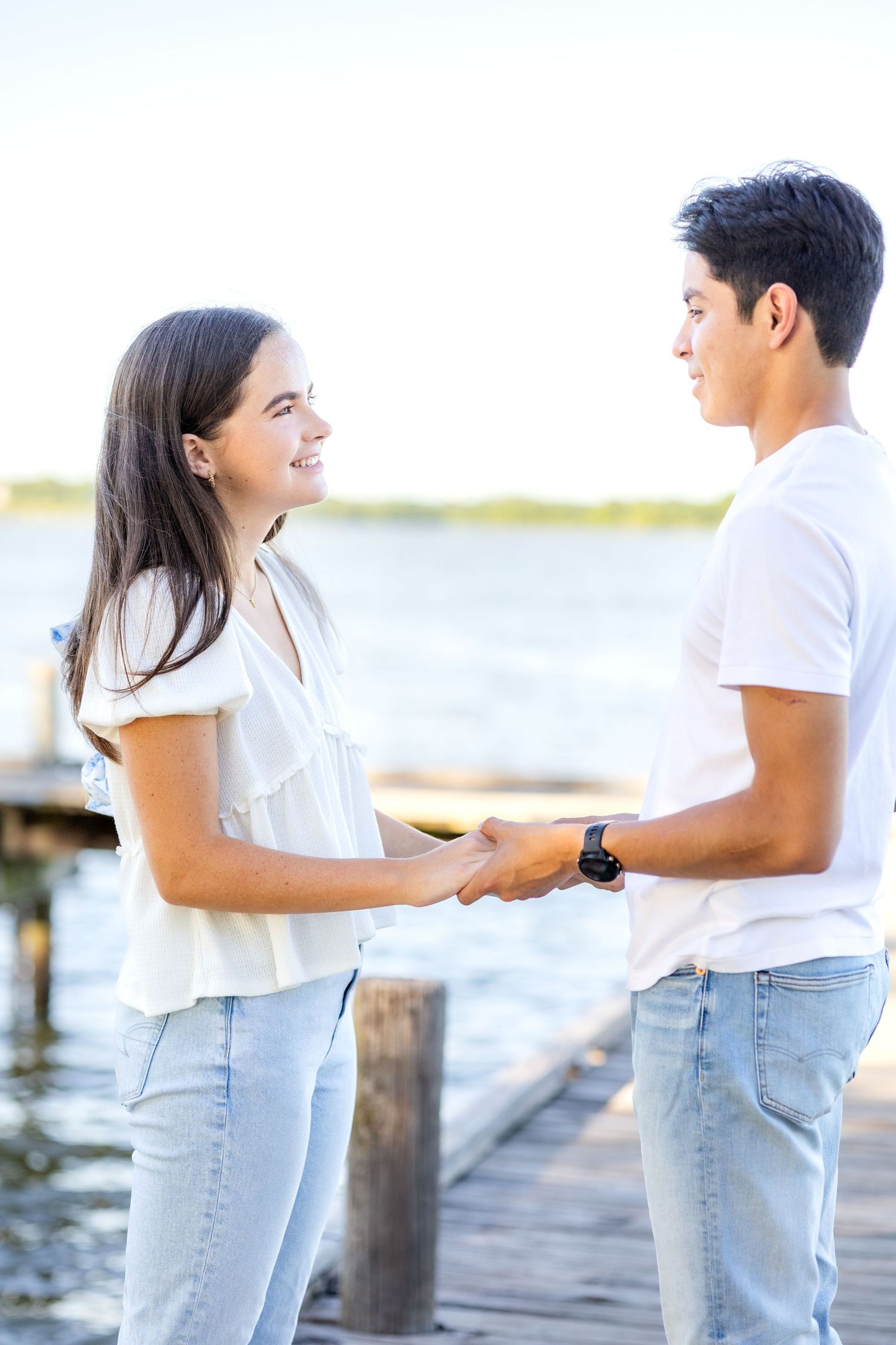 Engaged couple sweetly holding hands on the dock at White Rock Lake during engagement photo session in Dallas