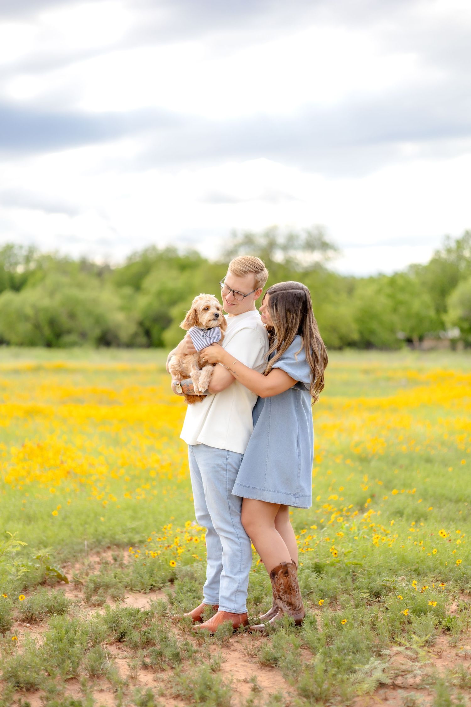 husband and wife standing in a wildflower field in Abilene, Texas with their Cavapoo puppy and petting him