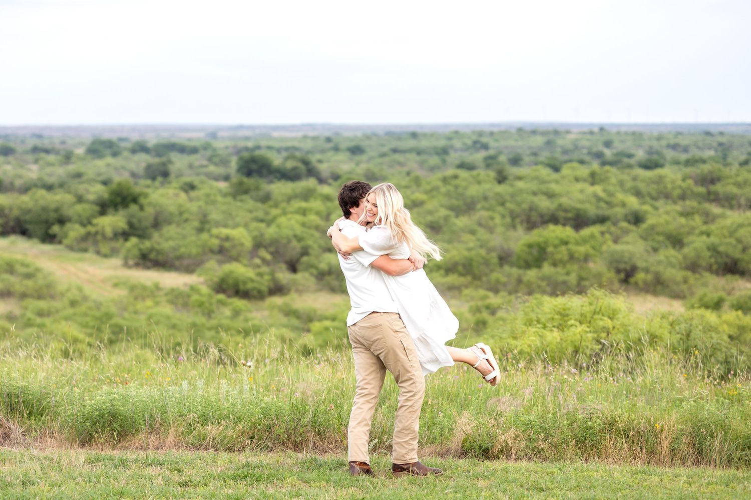 Engaged man picking up his fiancé and spinning her around like they have not seen each other in years during engagement photo session