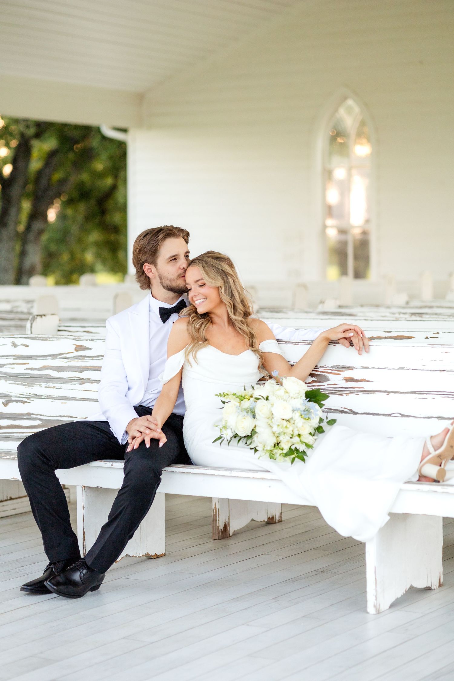 Bride and groom sitting and snuggled in next to each other on wedding chapel pew at Chandelier Farms at Dallas wedding