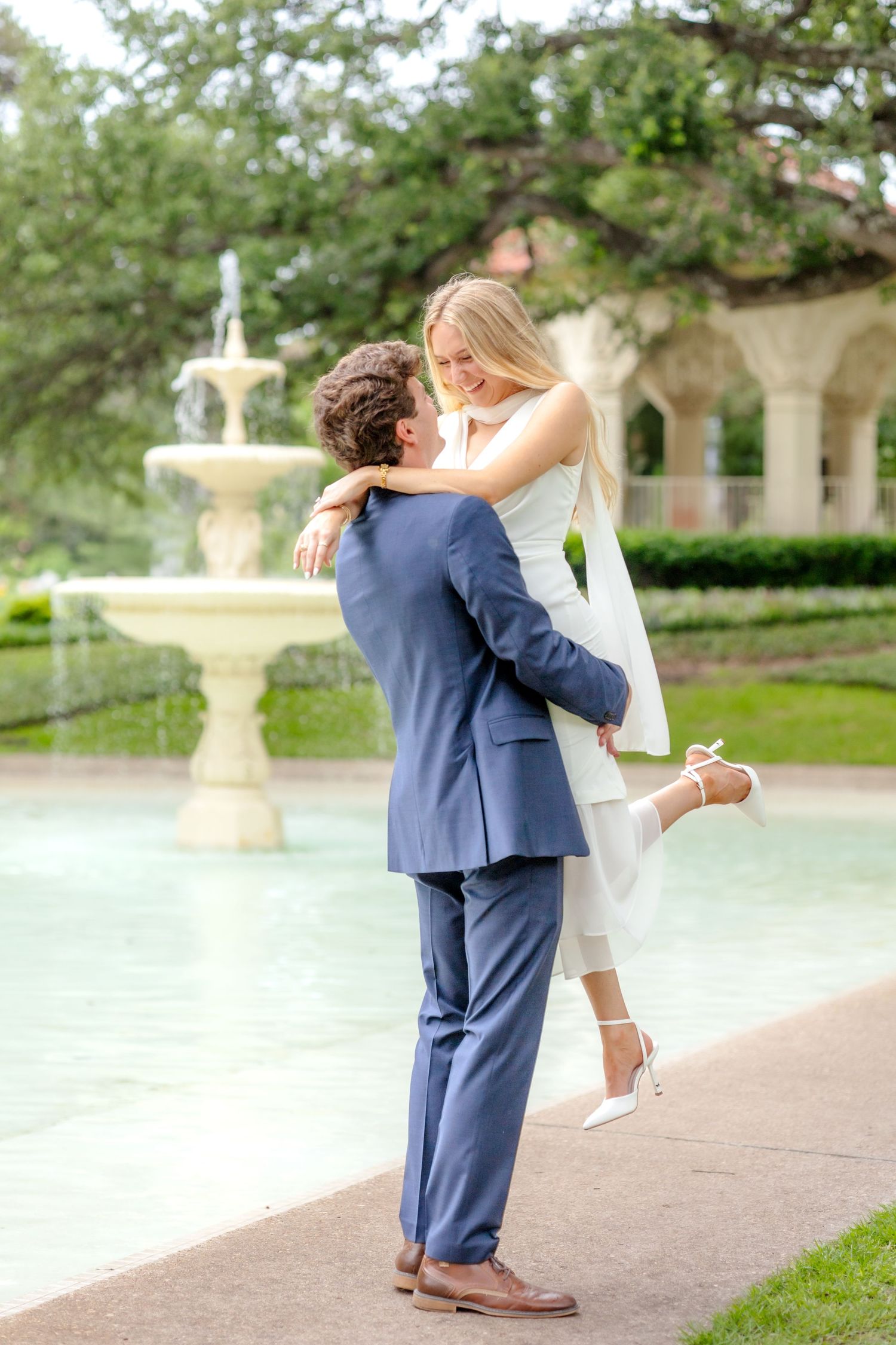 Engaged couple shares a romantic lift by the fountain at Flippen Park in Dallas, TX during their elegant engagement session.
